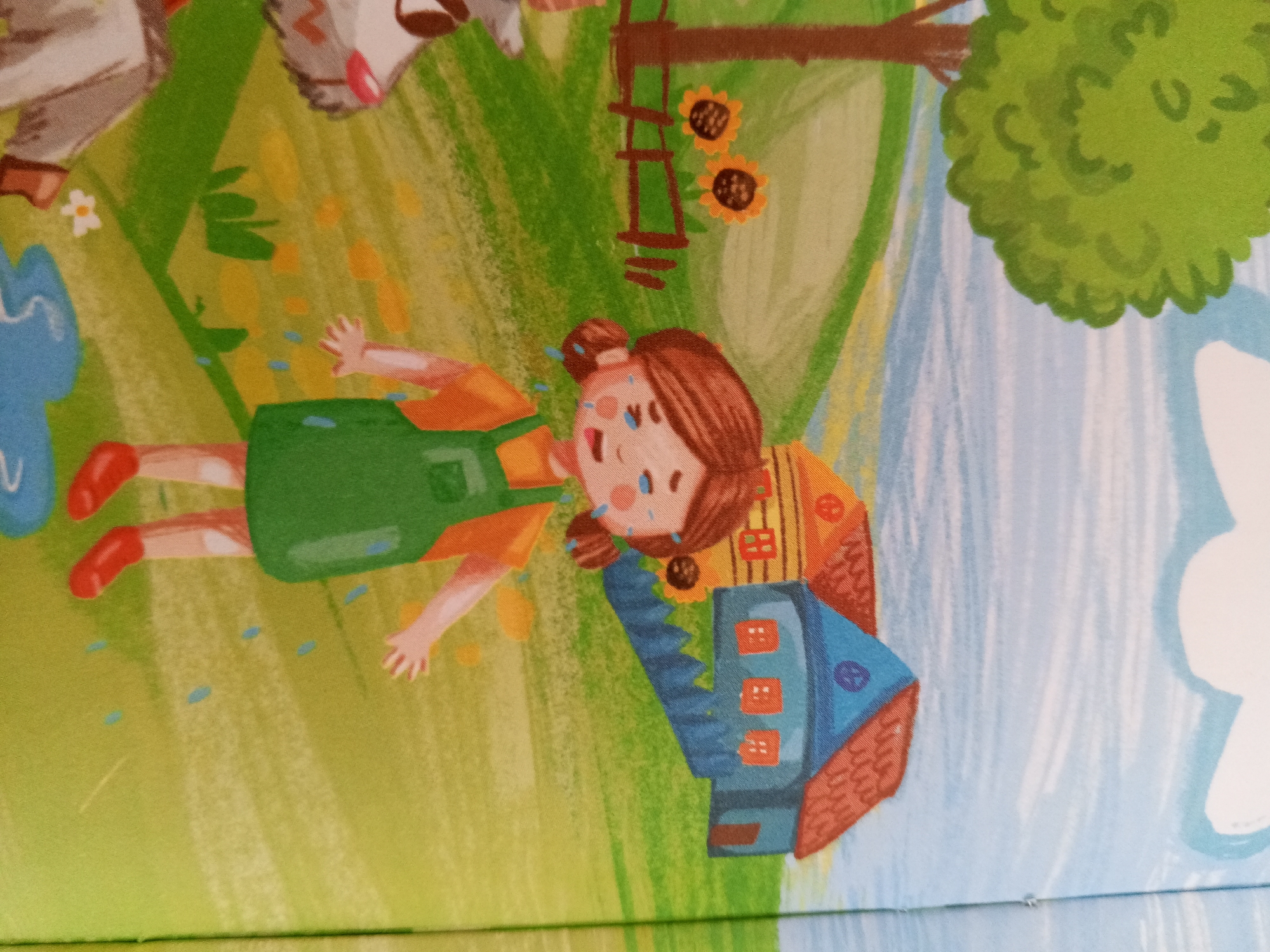 The image is a close-up of a colorful illustration depicting a cartoonish scene. In the foreground, a young girl with brown hair styled in two buns is lying on her back and crying. She is wearing an orange shirt and a green overall dress. There are light blue teardrop shapes scattered around her, suggesting she is upset. To the girl's right, a small blue and red house-like structure is partially visible. In the background, there is a green grassy area with yellow and green strokes, suggesting a field. A tree with a large green canopy is visible on the right side of the image. Two sunflowers are depicted hanging from a brown ladder-like structure in the upper middle of the image. A white flower and a blue blob are visible in the upper left corner. The overall image appears to be a page from a children's book or a similar artistic rendering. There is no identifiable information or context within the image that would allow for its location in Chistopol, Russia.