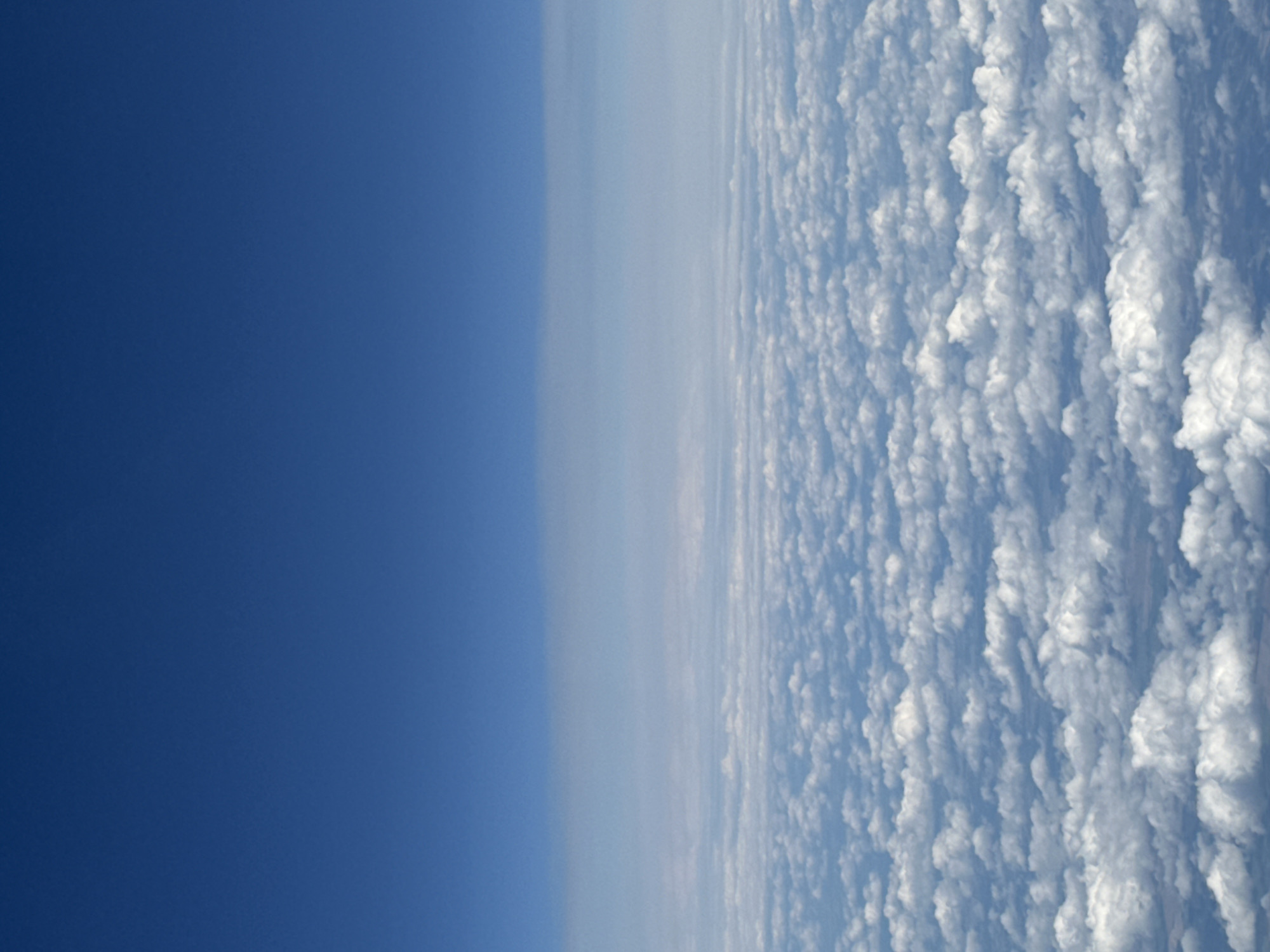 The image shows a vast expanse of white clouds from an aerial perspective. The sky above the clouds is a deep, clear blue. The clouds are densely packed, creating a textured, undulating surface that stretches to the horizon. There are no people, objects, or structures visible in the image. The scene appears to be a natural, atmospheric phenomenon. The location in Клейнікаўскі сельскі Савет, Belarus, is not determinable from the image itself, as it depicts a generic view of the sky and clouds.