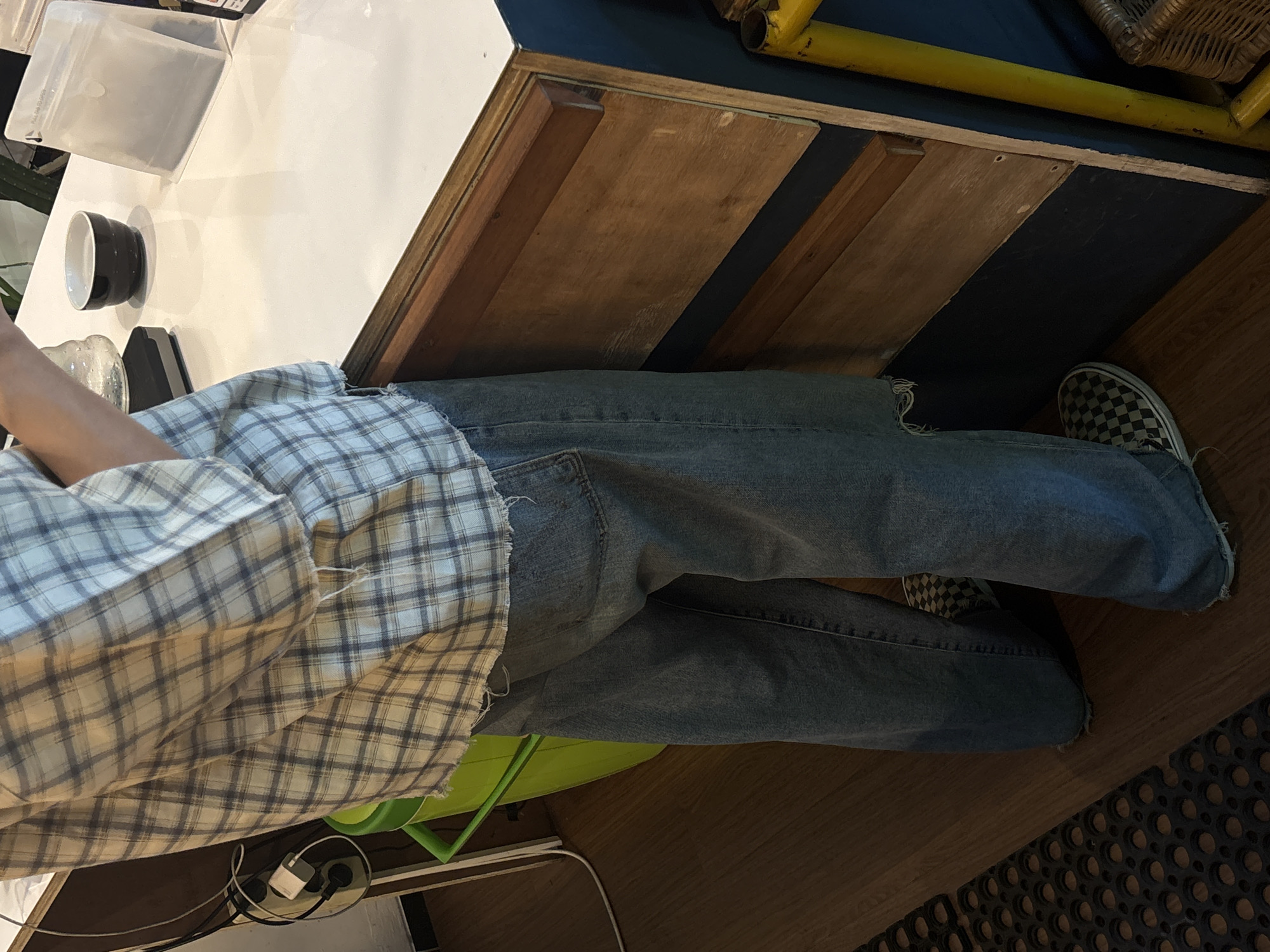 The image shows a person standing in front of a counter, possibly in a cafe or shop. The person is wearing a plaid shirt and loose-fitting jeans. The counter is made of wood and has a white top. On the counter, there are coffee-making equipment, a bowl, and a bag of coffee. The floor is made of wood. The scene appears to be indoors.
Without further information, it is not possible to determine the specific location in Semarang, Indonesia. However, given the context of coffee-making equipment, it is likely a cafe or a coffee shop. The overall ambiance suggests a casual and relaxed atmosphere.