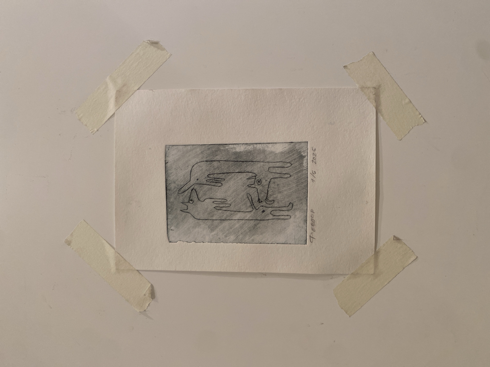 A small print is taped to a white wall with four pieces of masking tape, one in each corner. The print itself is a rectangular piece of paper with a gray image printed on it. The image depicts a stylized representation of animals or figures arranged in a horizontal composition. The signature "Feodor" and the numbering "1/5 2025" are visible on the right side of the paper. The overall scene suggests a personal or informal display, possibly within a home or studio setting. There is no indication of Moscow, Russia.