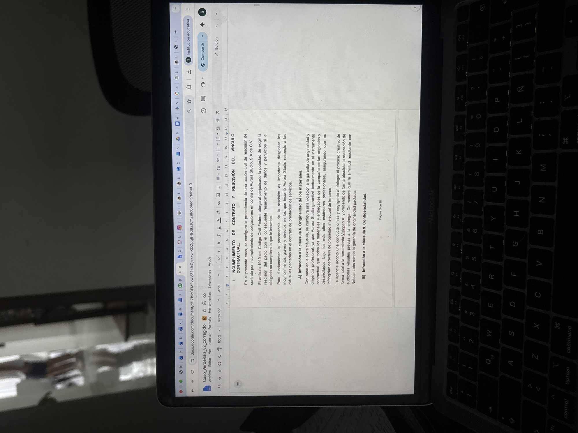 Here's a matter-of-fact description of the image:
**Scene:** A laptop, likely a MacBook Air, is open and displaying a Google Docs document. The document is in Spanish and appears to be a legal document or contract, titled "Caso_VerdeRaiz_v2_corregido". The content discusses the breach and termination of a contractual link, specifically citing non-compliance and potential legal action against "Aurora Studio". It mentions clauses regarding originality of materials and confidentiality.
**Objects:** A portion of a chair is visible on the left side of the image, indicating the laptop is resting on a surface. The laptop's keyboard is visible. The laptop is in an indoor location.
There is no information in the image to indicate this photo was taken in San Bernardino Tlaxcalancingo, Mexico.
