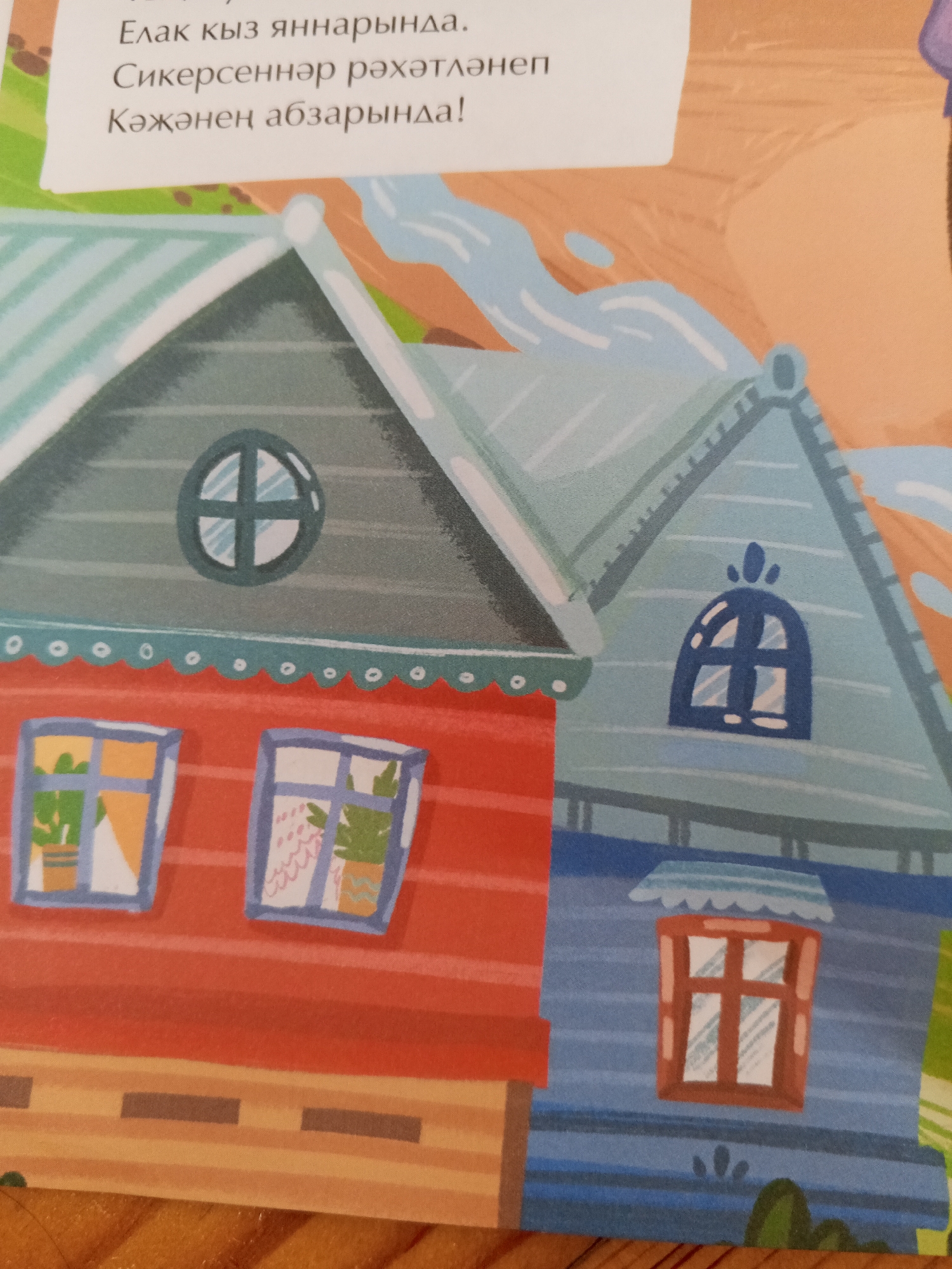 This is a brightly colored illustration of two houses, one red and one blue, with a river or stream flowing behind them. The houses have various windows, some with plants visible inside. The overall style is cartoonish and cheerful. Text in an unfamiliar language is visible at the top of the image. The prompt asks for a description including the location in Chistopol, Russia, but there is no visual information within the image itself that would indicate this specific location. Therefore, I cannot provide details about Chistopol, Russia based solely on the image.