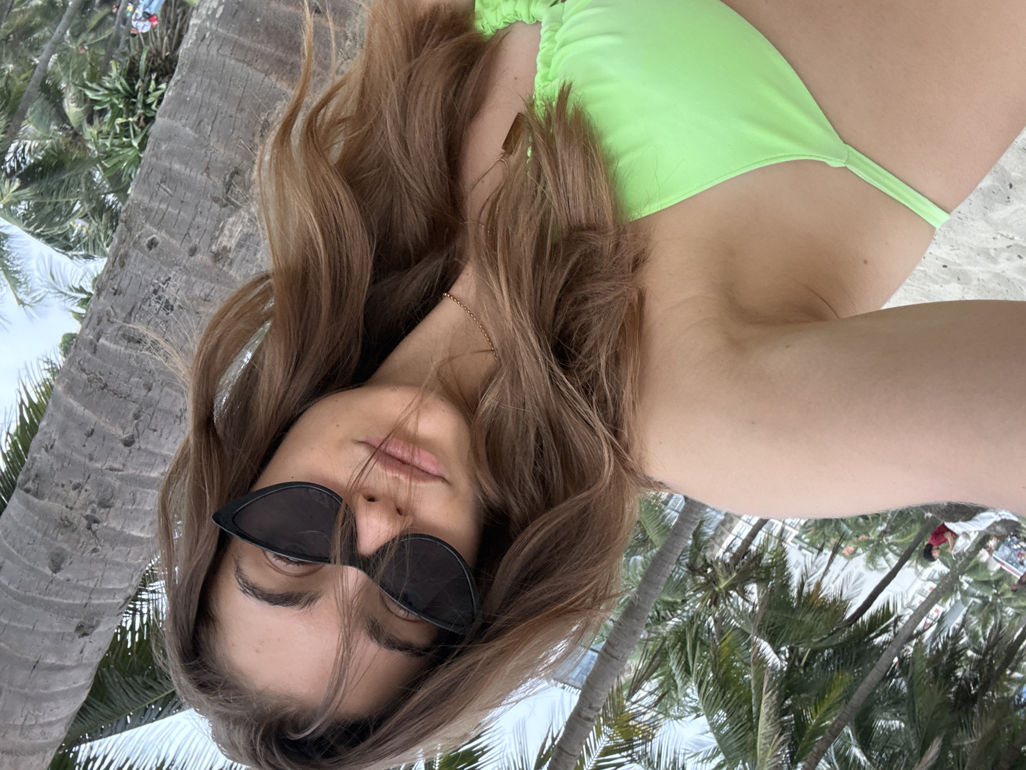 A woman in a green bikini and black sunglasses lies on a beach under palm trees. The location is Đà Nẵng, Vietnam.