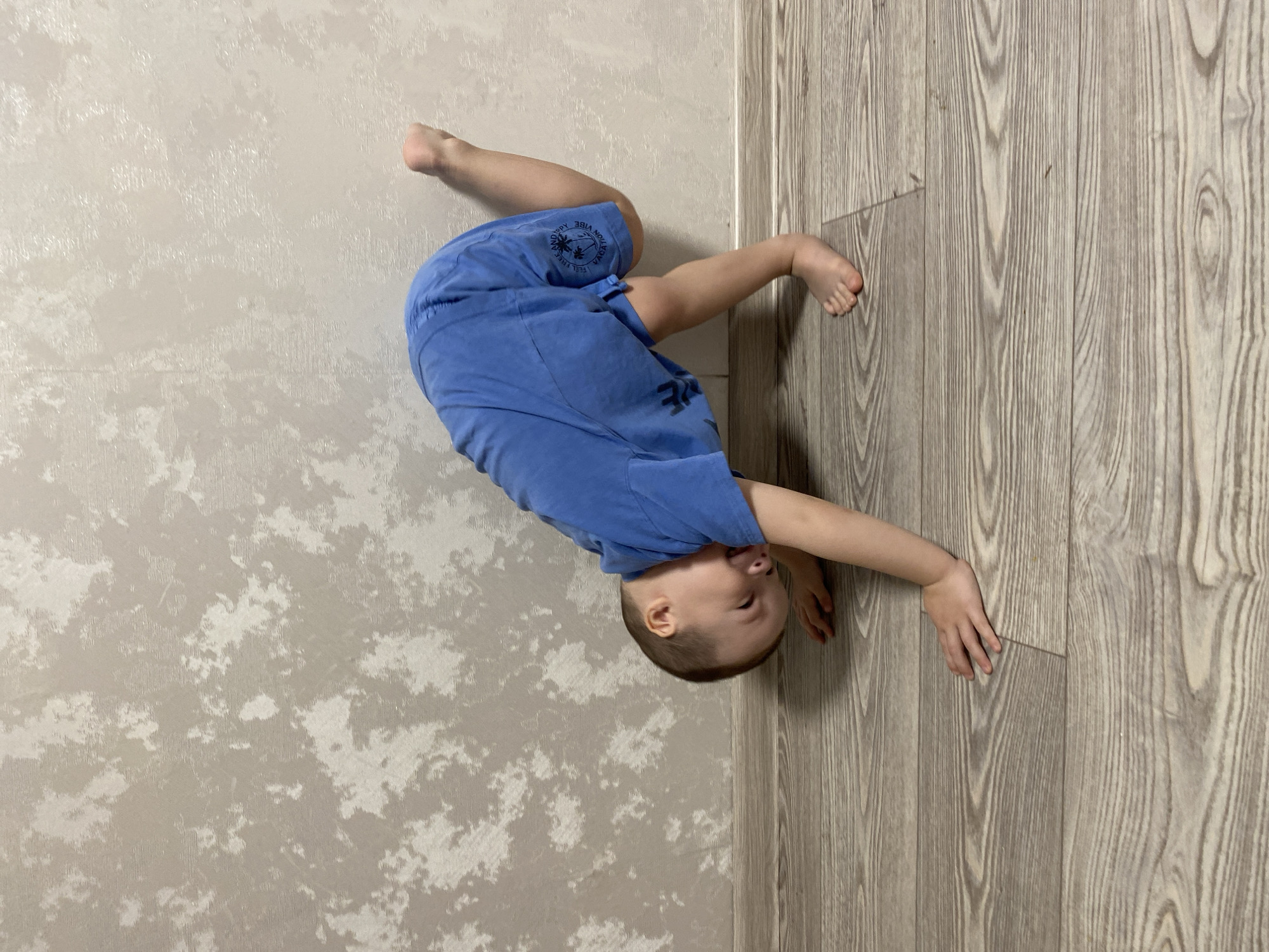A young child wearing a blue shirt and shorts is positioned upside down, with feet near a textured wall and hands touching a wooden-look floor. The location is indicated to be Sochi, Russia.