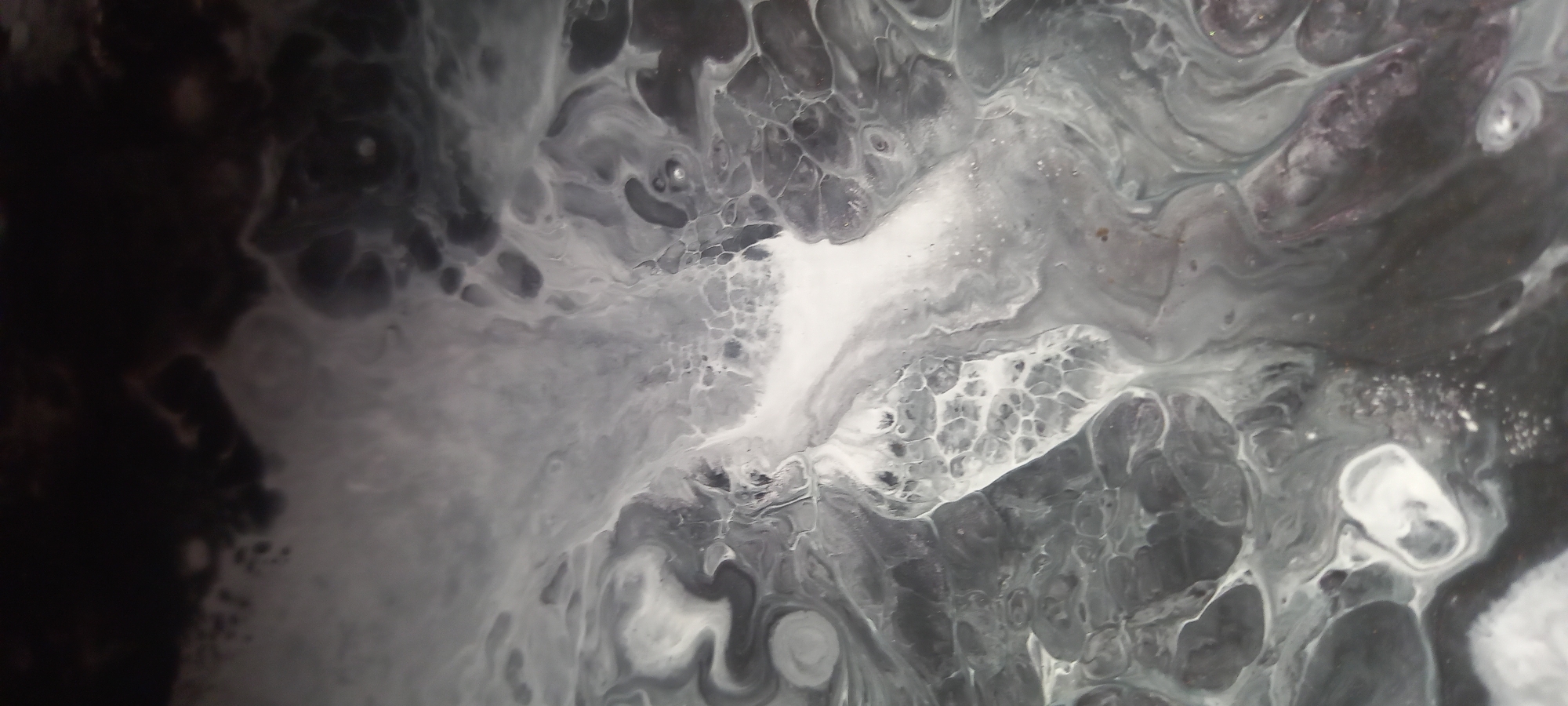 This is an abstract, close-up image of what appears to be a fluid art painting. The colors are predominantly black, white, and shades of gray, with some subtle hints of metallic or iridescent particles. The textures are varied, with smooth, flowing lines of paint interspersed with cellular or bubbly patterns. There are no discernible objects, people, or actions, and the scene does not provide any information about the city of Kryvyi Rih, Ukraine.