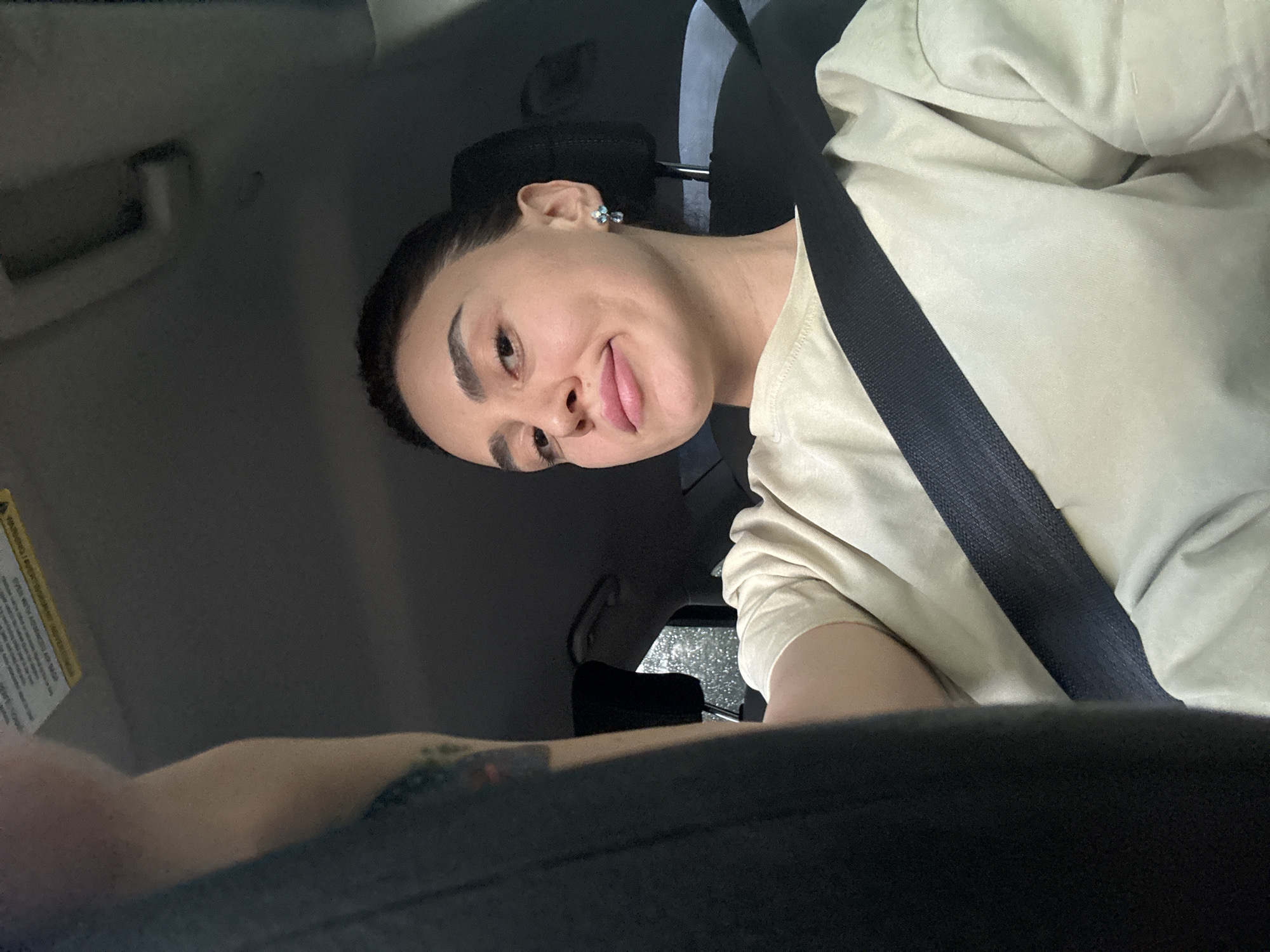 A person wearing a seatbelt and a light tan shirt sits in a vehicle. Rain can be seen on the vehicle's rear window. The location is likely Tbilisi, Georgia.