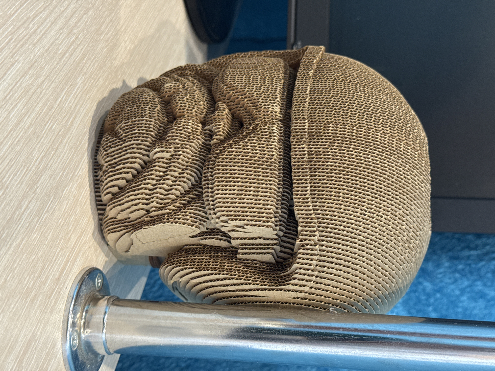 A layered cardboard sculpture of a human head rests on a metal railing. The background shows a light wooden panel and a dark-colored structure with blue accents. The location, Chuprino, Russia, is not evident from the image.