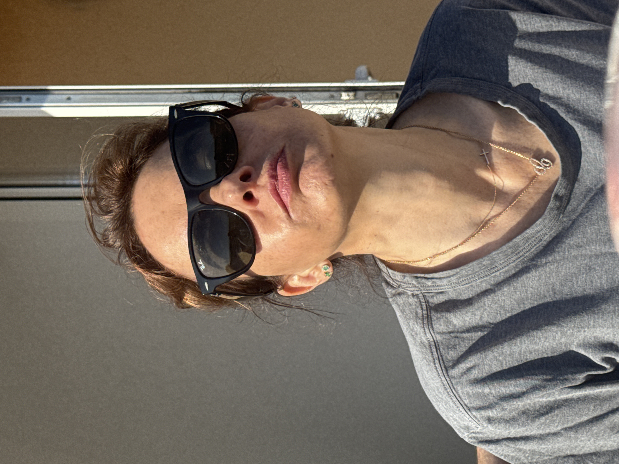 A woman with sunglasses, wearing a gray t-shirt and a gold necklace, is photographed in an outdoor setting. The location and city details (Vila Nova de Gaia, Portugal) are not identifiable from the visual information available in the image.