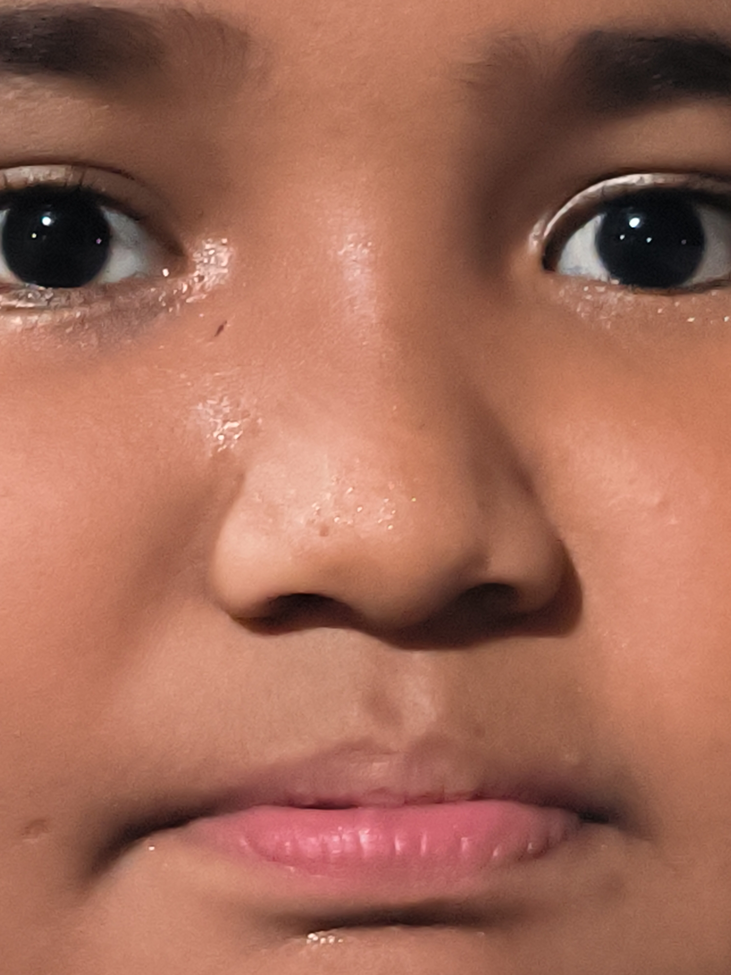 A close-up of a person's face, focusing on the eyes, nose, and mouth. The person has dark eyes with white eyeliner on the upper eyelid. The skin has a slightly shiny appearance. The lips are pink. The location is not discernible.