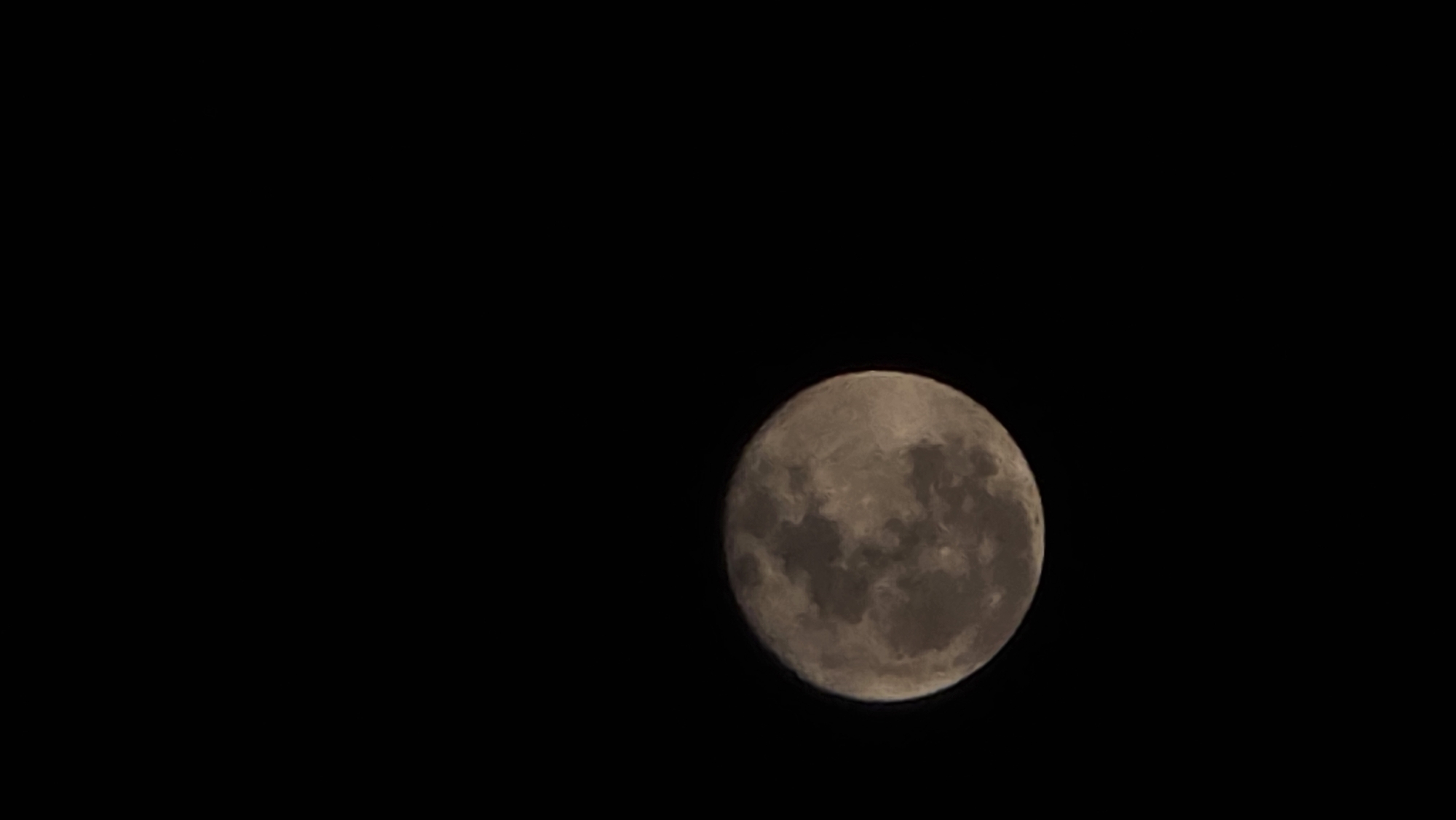 A full moon dominates the right side of a black background. The moon's surface displays variations in shading, suggesting craters and other lunar features. The black background fills the rest of the frame. The image provides no clues regarding location or the presence of people or other objects beyond the moon.