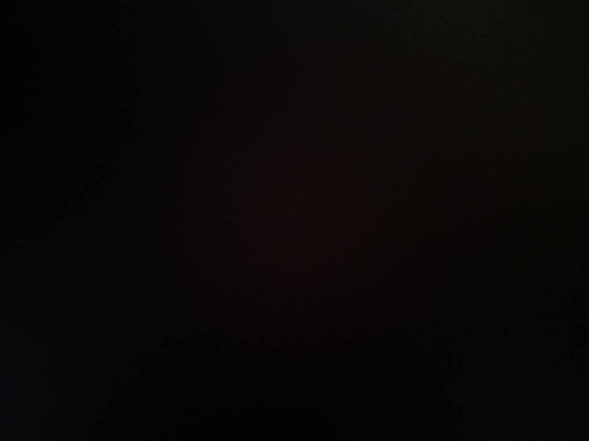 The image is a very dark, almost entirely black frame with some faint, reddish-brown hues visible, particularly towards the bottom right. There are no discernible subjects, objects, or activities. The lack of detail suggests it could be a picture taken in extremely low light conditions, possibly at night or indoors with no light source. There is no visible text. The location context of Belgrade, Serbia, does not provide any further clues given the abstract nature of the image.