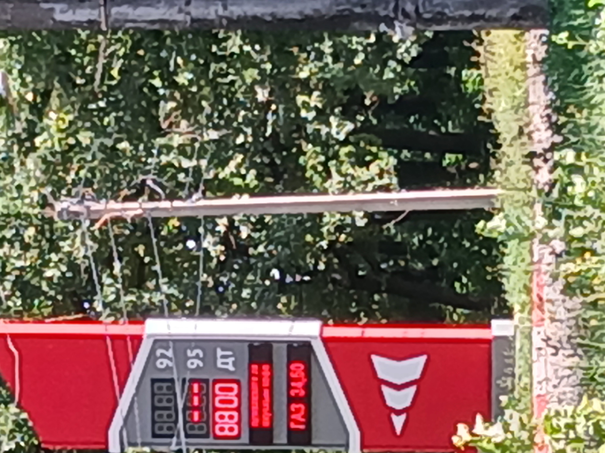 A red and gray gas price sign is visible at a gas station in Lipetsk, Russia. The sign displays prices for different types of fuel. The top section shows "88.88" next to "92", and "88.88" next to "95". Below that, "88.00" is shown next to "ДТ". Further down, "ГАЗ 34,50" is displayed. The background consists of green trees and a utility pole.