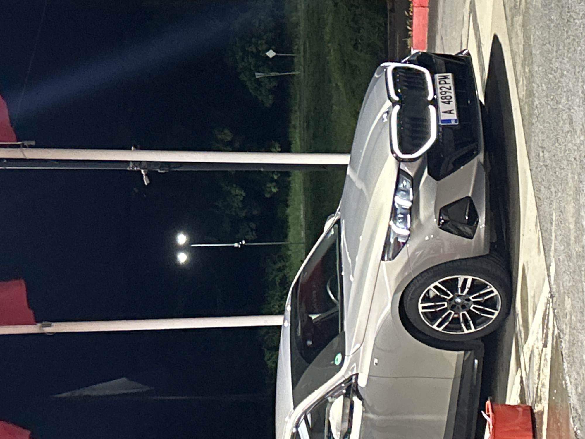 The image shows a silver BMW parked near a street light at night. The license plate reads "A 4892 PM". Based on the license plate prefix "A", the vehicle is likely registered in Burgas, Bulgaria. The environment appears to be a street in Burgas.