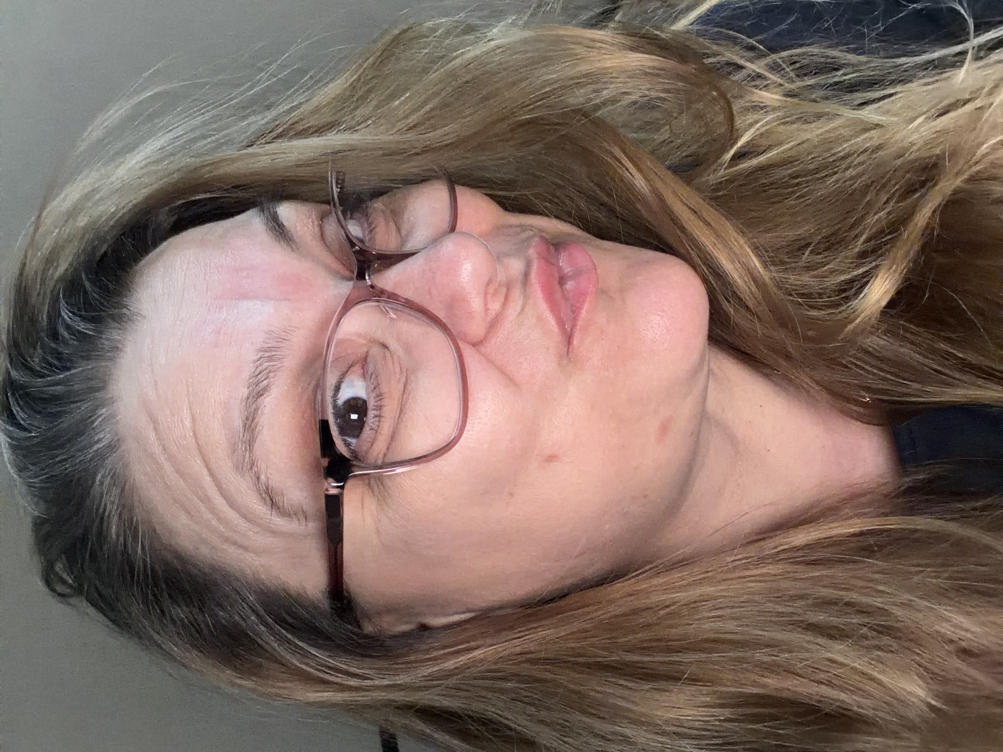 A close-up selfie of a woman with light brown hair and glasses. Her head is turned to the left, and she is puckering her lips. The background is a plain gray wall. The image does not contain any identifiable landmarks or features that would allow for its location to be determined within Southend-on-Sea, United Kingdom.