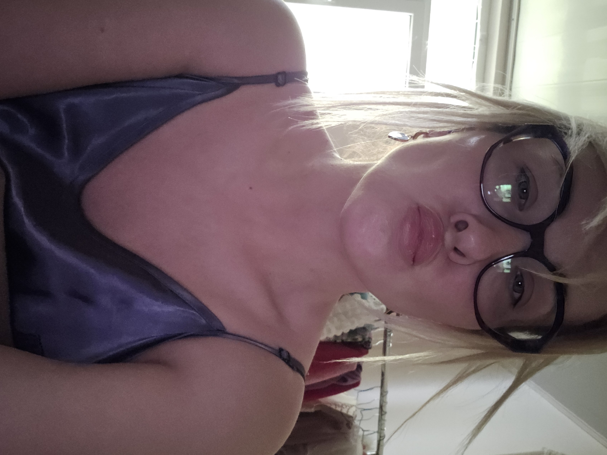 A pale-skinned woman with blonde hair is wearing eyeglasses and pouting her lips. She is wearing a camisole. A window is visible in the background. It is impossible to determine the location of the image as Sochi, Russia, from the given information.