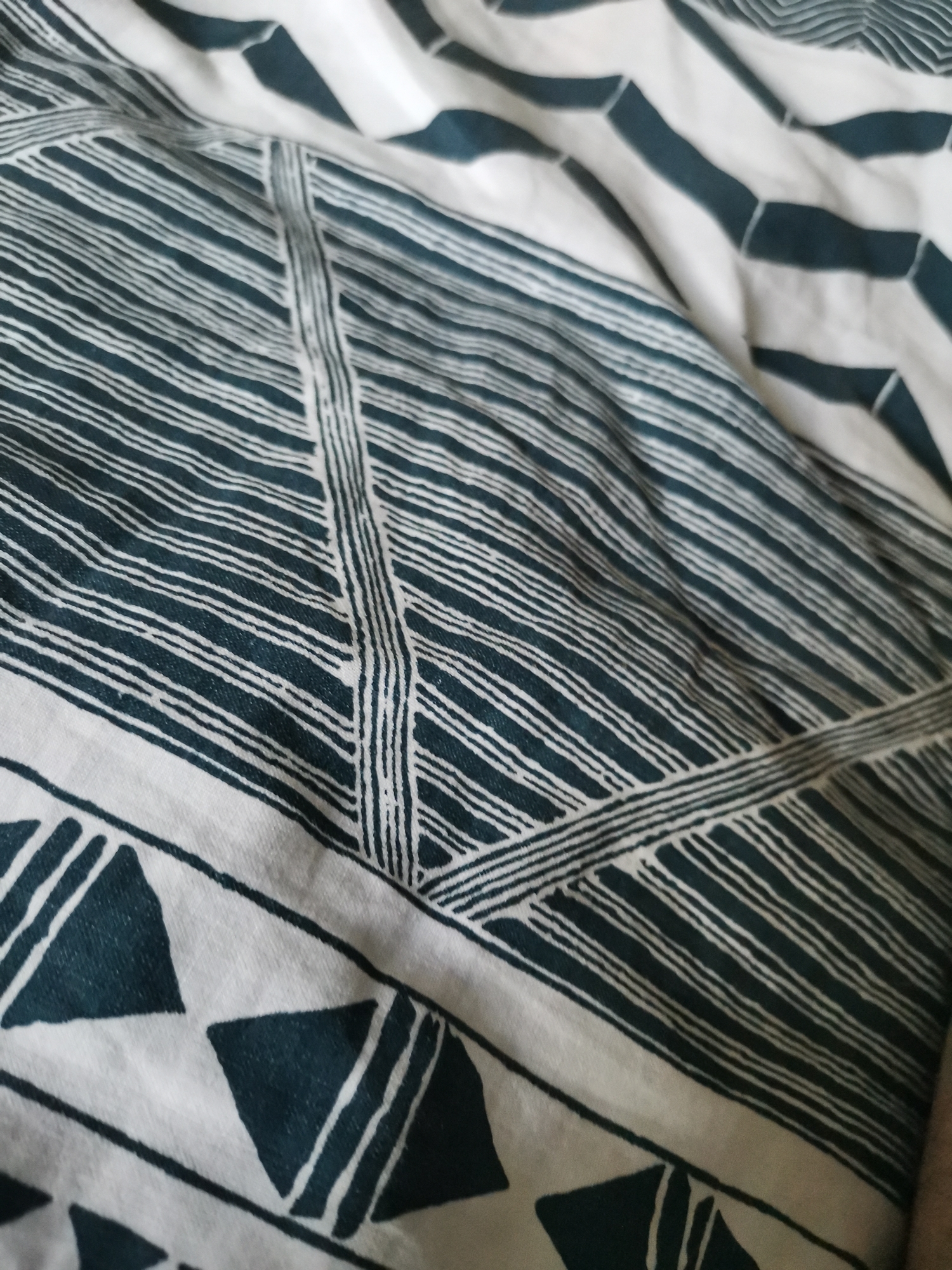 The image shows a close-up of patterned bedding. The fabric is white with a dark teal or blue-green geometric design. The pattern includes stripes, triangles, and chevron-like shapes. The fabric is wrinkled. There are no people or other identifiable subjects. The location in Pokrovnik, Bulgaria is unknown given the information provided.