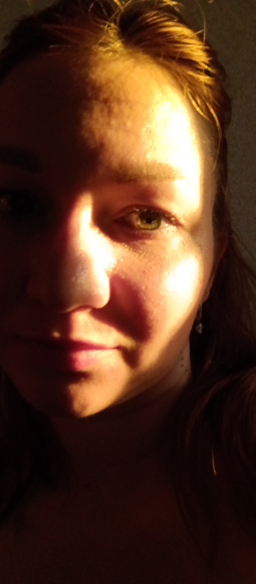 A close-up photograph depicts a person's face partially illuminated by strong, possibly artificial, light. The light source casts harsh shadows, obscuring portions of the face, notably the left side of the face and the lower region of the chin. The person has fair skin, light-colored hair, and green-colored eyes. There is no information available about the location or the city from the image provided.