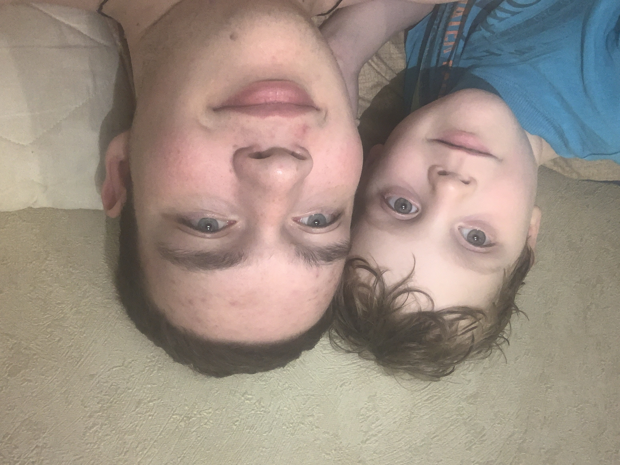 Two individuals, presumably a teenager and a child, are positioned close together, their heads nearly touching. They are lying on a surface, likely a bed or couch, covered with a textured, light-colored material. The teenager is positioned on the left, and the child is on the right. The teenager has a light complexion, short dark hair, and blue eyes. The child also has a light complexion, brown hair, and blue eyes.
There is no indication of the location being Severodvinsk, Russia, in the image.