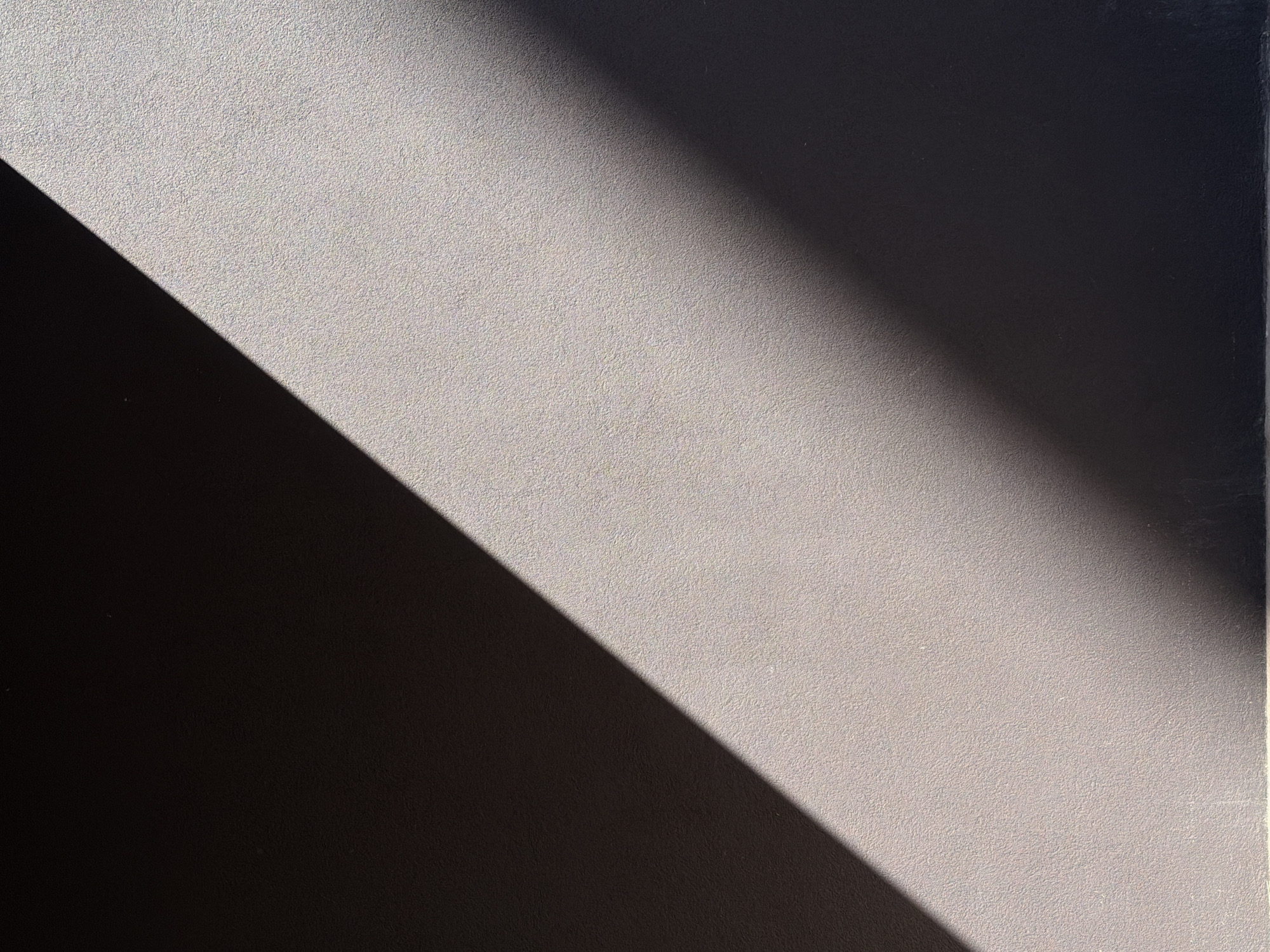 The image shows a section of a wall with a diagonal band of shadow across it. The wall appears to have a textured surface, and the light suggests an outdoor setting. The location in the city of Belgrade, Serbia is not identifiable from the provided image. There are no people, subjects, objects, actions, or interactions that are visible other than the shadow. The environment seems to be a building surface.