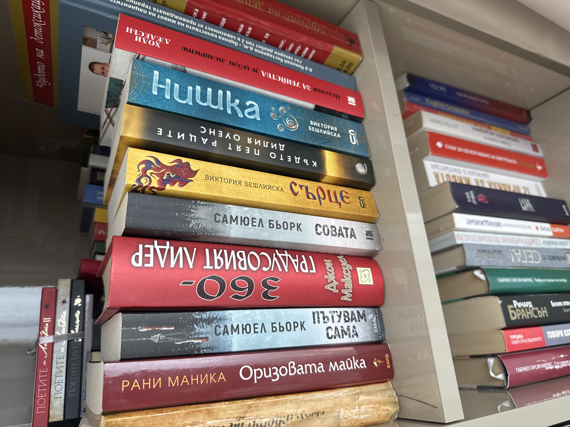 The image shows a close-up view of a bookshelf filled with books. The books are of various colors and sizes, with some standing upright and others leaning against each other. The bookshelf itself appears to be made of light-colored material, possibly particleboard or laminate, with a visible seam running across the middle shelf. The overall impression is one of a private collection of books, likely in a home or office setting.
While the prompt requests a description including the location in Burgas, Bulgaria, this information cannot be determined from the image alone. The image does not contain any visual cues or text that would associate it with a specific geographical location, including Burgas. Therefore, any mention of Burgas would be speculative and not based on the visual evidence present.