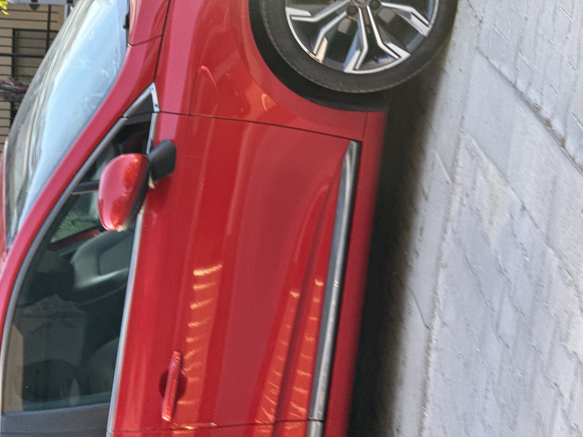 The image shows a close-up of a red car parked on a paved surface. The car's front wheel is visible, along with the driver's side door, window, and side mirror. The inside of the car is partially visible through the window. The image does not provide enough information to determine the specific location in Sofia, Bulgaria. There are no people visible in the image.