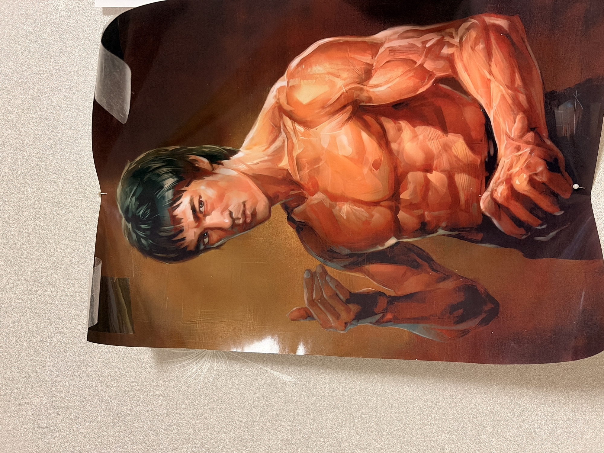 This is a medium shot, eye-level photograph of a poster of Bruce Lee, a martial artist and actor, hanging on a wall. The poster is a painting depicting Bruce Lee in a dynamic pose, showcasing his muscular physique. He has dark hair and a serious expression. The poster is attached to a textured, light-colored wall with clear tape at the top and a white thumbtack at the bottom. The lighting appears to be warm and directional, creating highlights and shadows on Bruce Lee's body and the poster's surface. The background of the poster is a gradient of warm tones, from a golden yellow to a dark brown. There is no visible indication of the city of Leninogorsk, Russia, in the image itself.