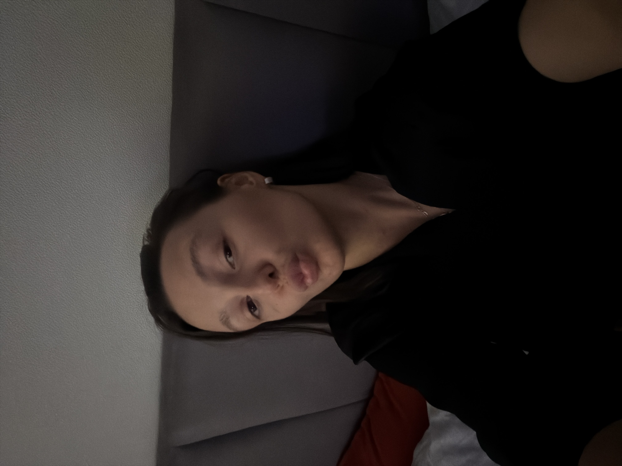 A young woman is lying down, possibly on a sofa or bed. She is wearing a black shirt. The background shows a plain wall. The scene takes place indoors. The location in the city of Khimki, Russia is not discernible from the image.