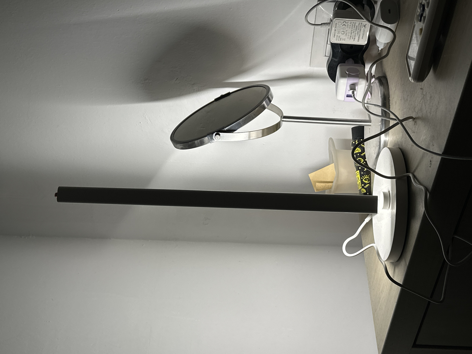 This image shows a desk with a makeup mirror and electronic devices plugged into a power strip. A remote control and other miscellaneous items are also present. The location, Ramat Gan, Israel, is not directly discernible from the image.