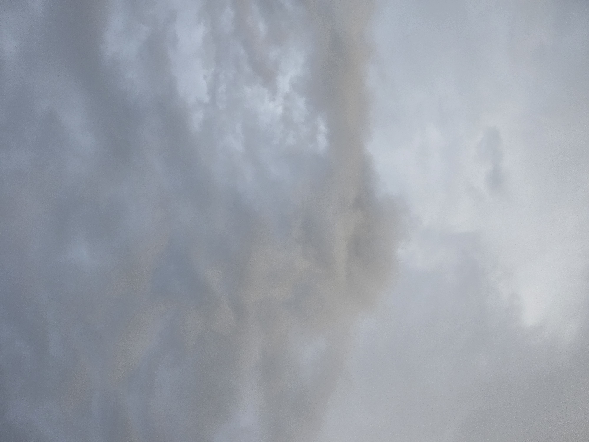 The image shows an overcast sky with layers of grey and white clouds. The location is unspecified and unknown. No people, subjects, or objects are visible other than clouds. There are no actions or interactions depicted. The environment is characterized by the cloudy sky.