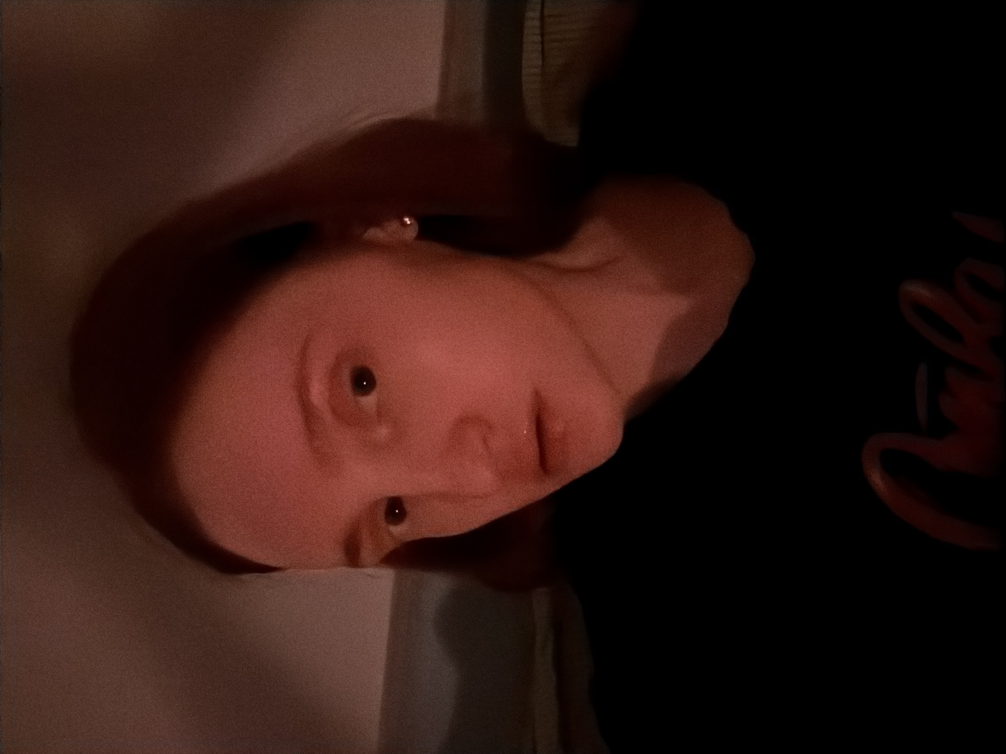 A close-up portrait of a fair-skinned person with auburn hair, wearing an earring, and a dark shirt. The person is facing the camera, and the image is slightly rotated counterclockwise. The background is dark and indistinct. There is no evidence to suggest the location is Boreti, Montenegro.