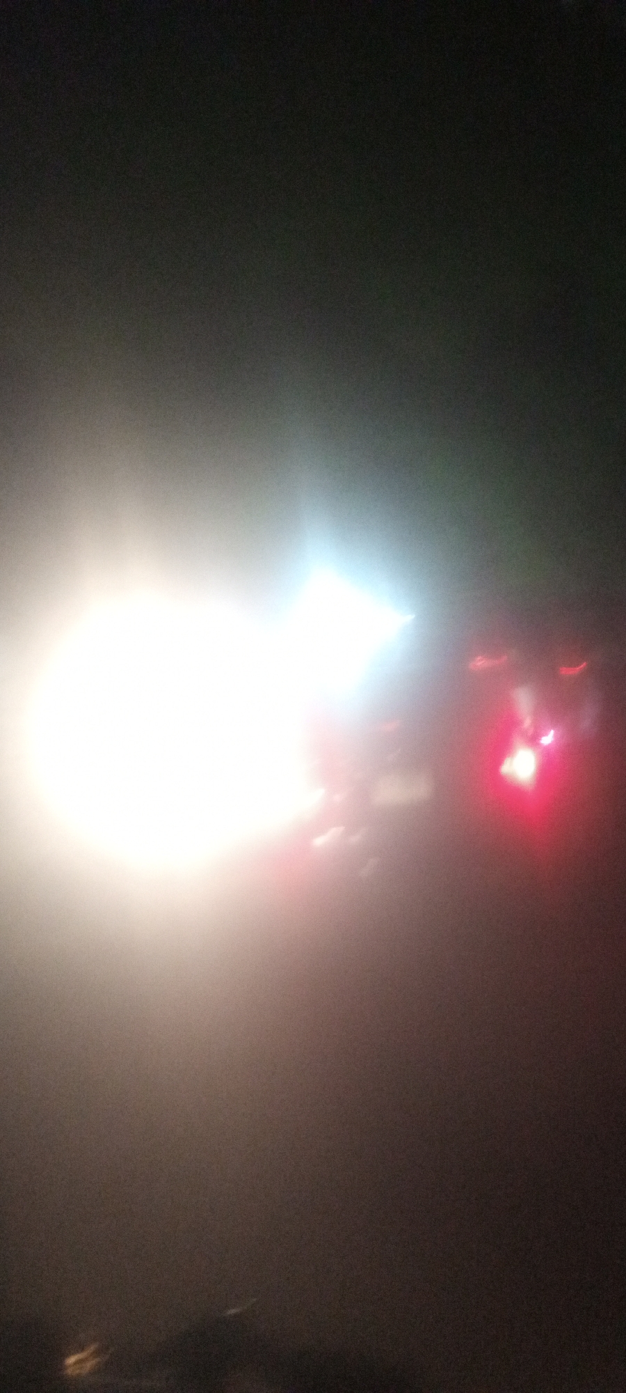 The image shows a blurred scene, likely captured at night in a dark environment. The dominant features are intense white and red lights, which may originate from vehicle headlights and taillights. The lights are diffused, possibly due to fog or poor visibility. The overall lack of detail and blurry nature of the image make it difficult to discern specifics about the location or any other elements present. There is no information in the image to ascertain that the location is specifically in Narayi, Nigeria.