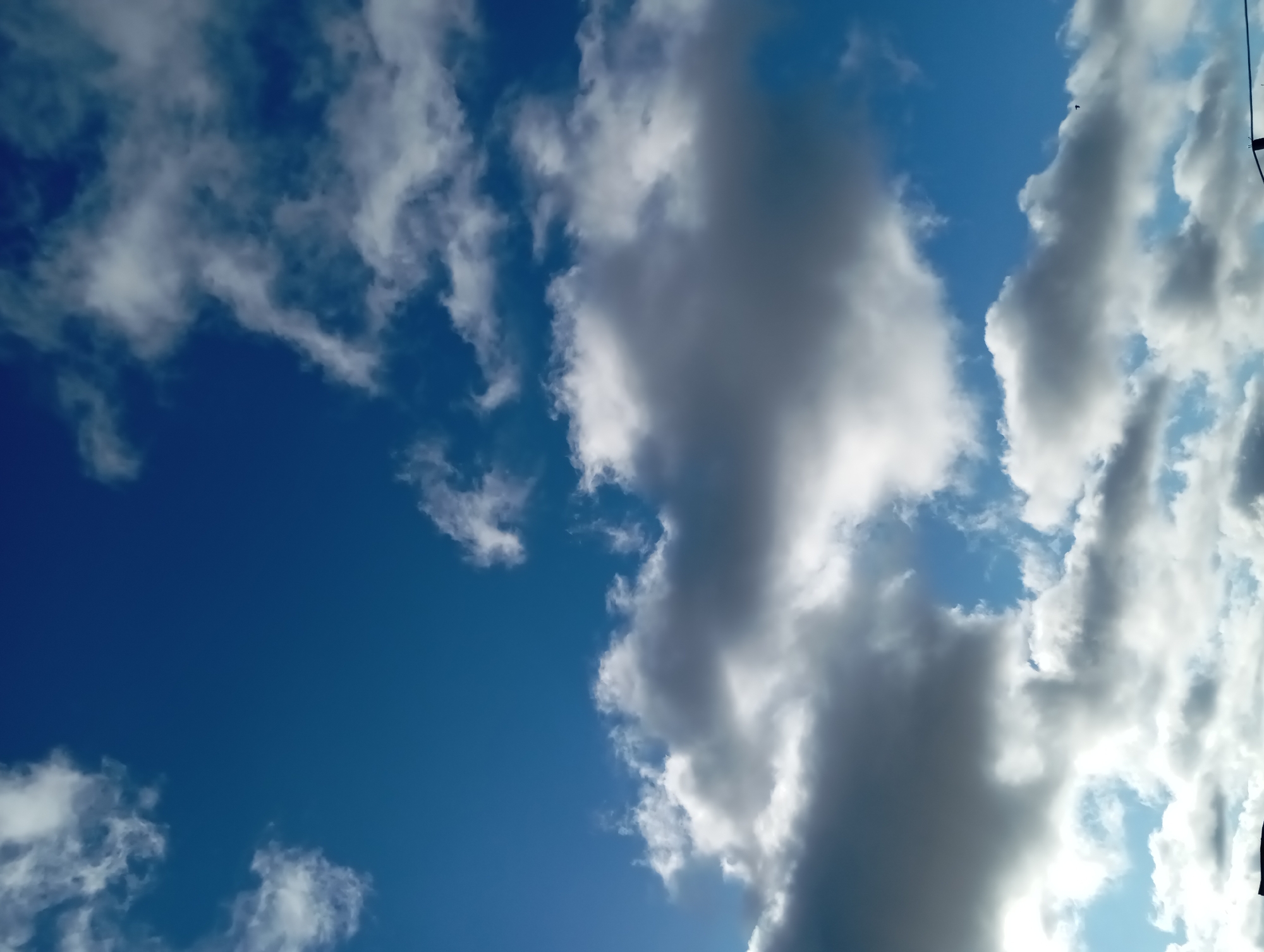 The image shows a daytime sky with blue patches and scattered cumulus clouds. The clouds range in color from bright white to dark gray, suggesting varying density and sunlight penetration. The image does not provide any information about the location or objects in the city of Yurgamysh, Russia. The scene shows clouds in the sky.