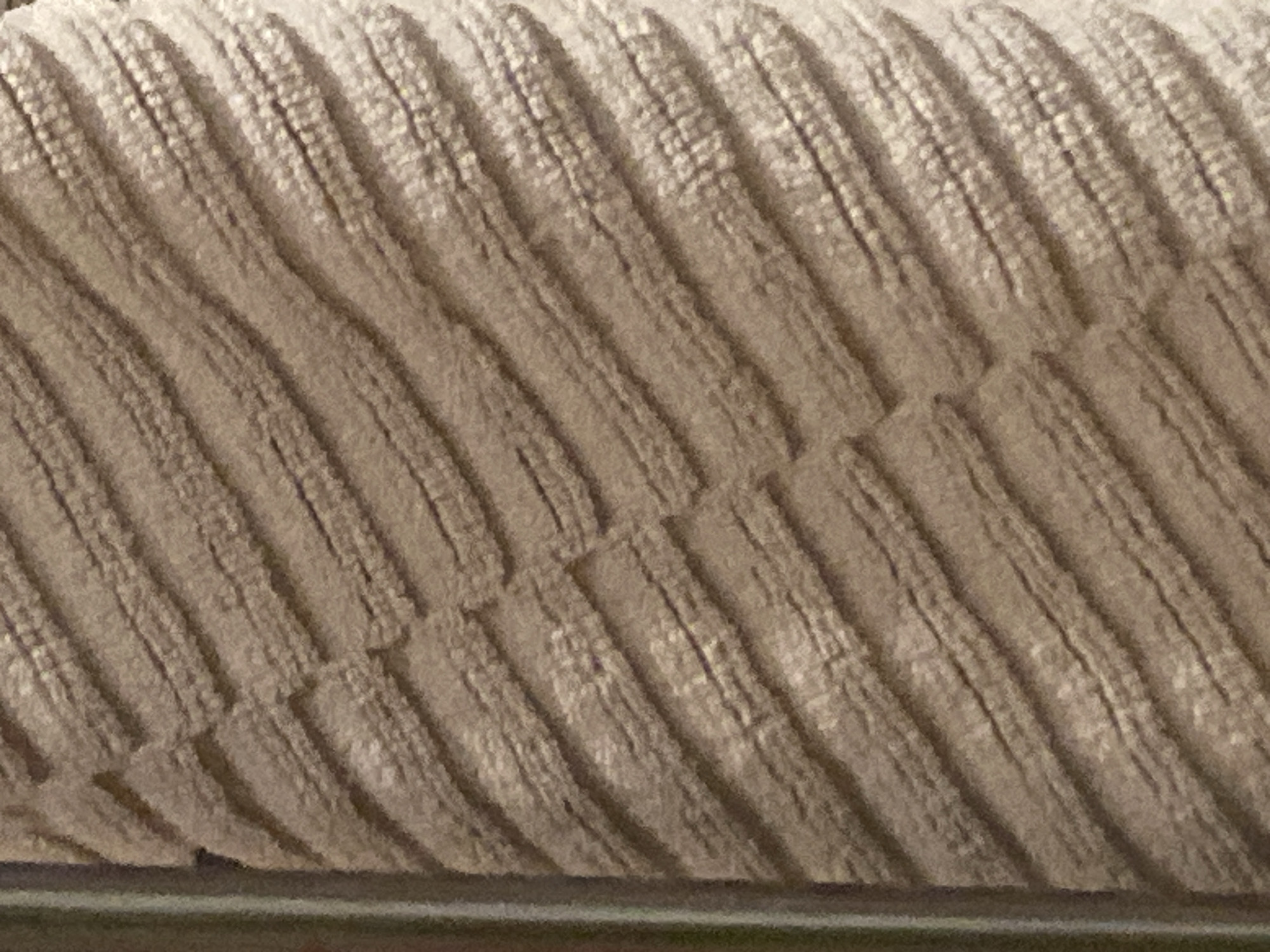 The image shows a close-up of beige corduroy fabric. The ribbed texture of the corduroy is clearly visible. The fabric appears to be resting on a horizontal metallic or dark-colored bar.
There are no people or recognizable objects other than the fabric. There is no indication of the location being Sofia, Bulgaria.