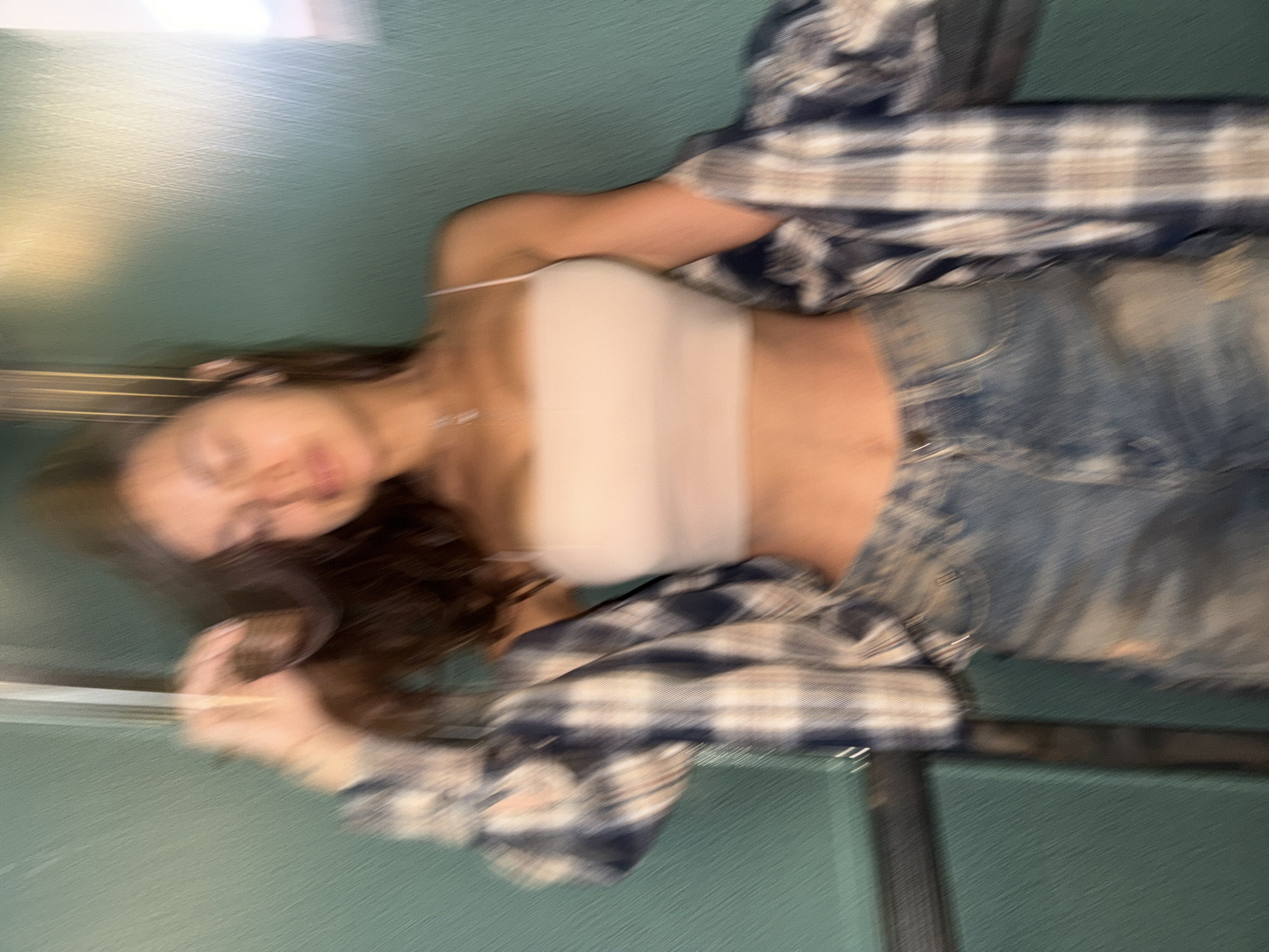 A blurry image shows a person wearing a light-colored crop top, denim jeans, and a flannel shirt, lying on what appears to be a green surface. The location in Krasnoyarsk, Russia is not discernable from the image.