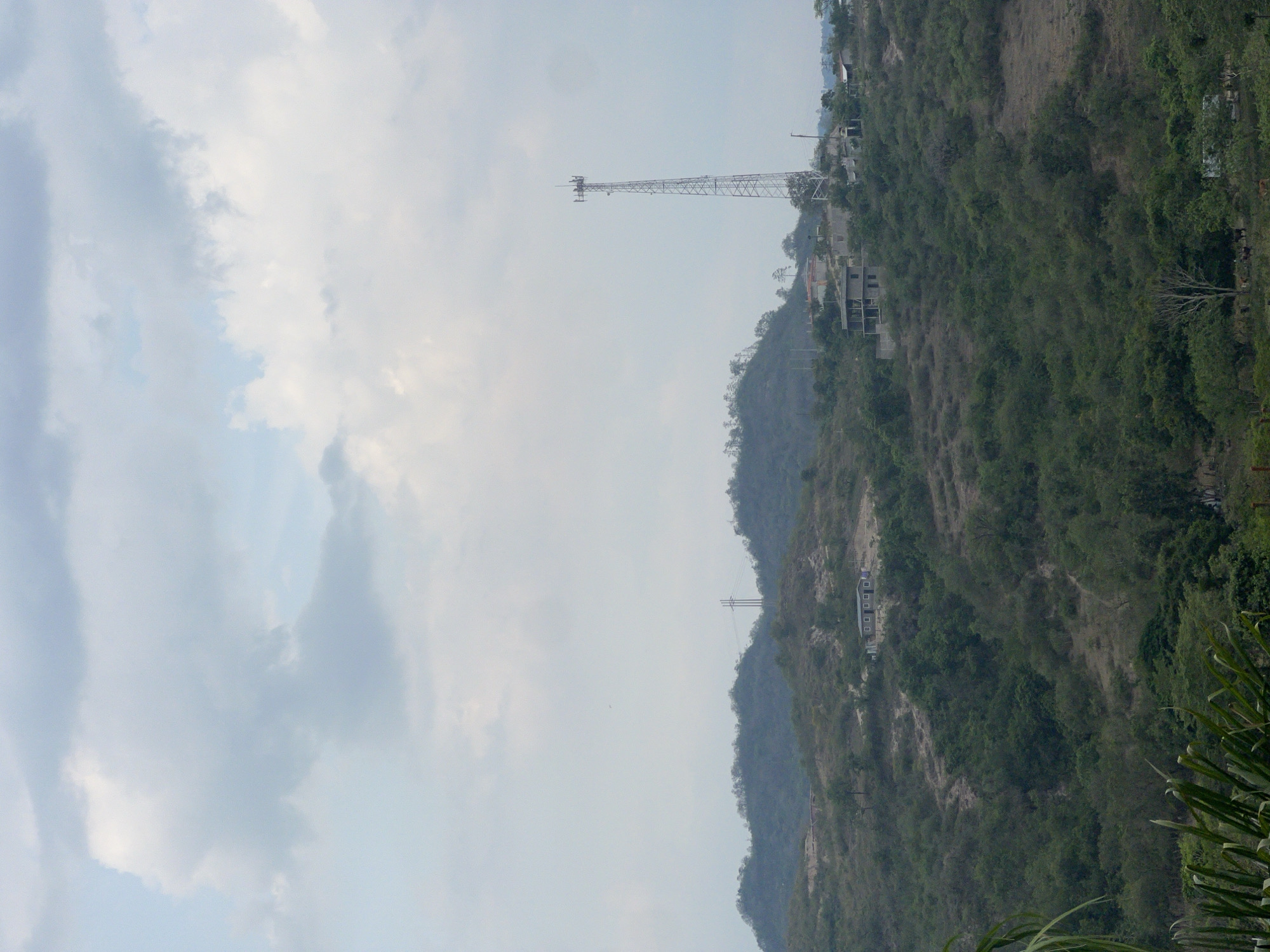 The image shows a hillside landscape with a communication tower and buildings. The sky is cloudy. It is located in the city of Gracias, Honduras.