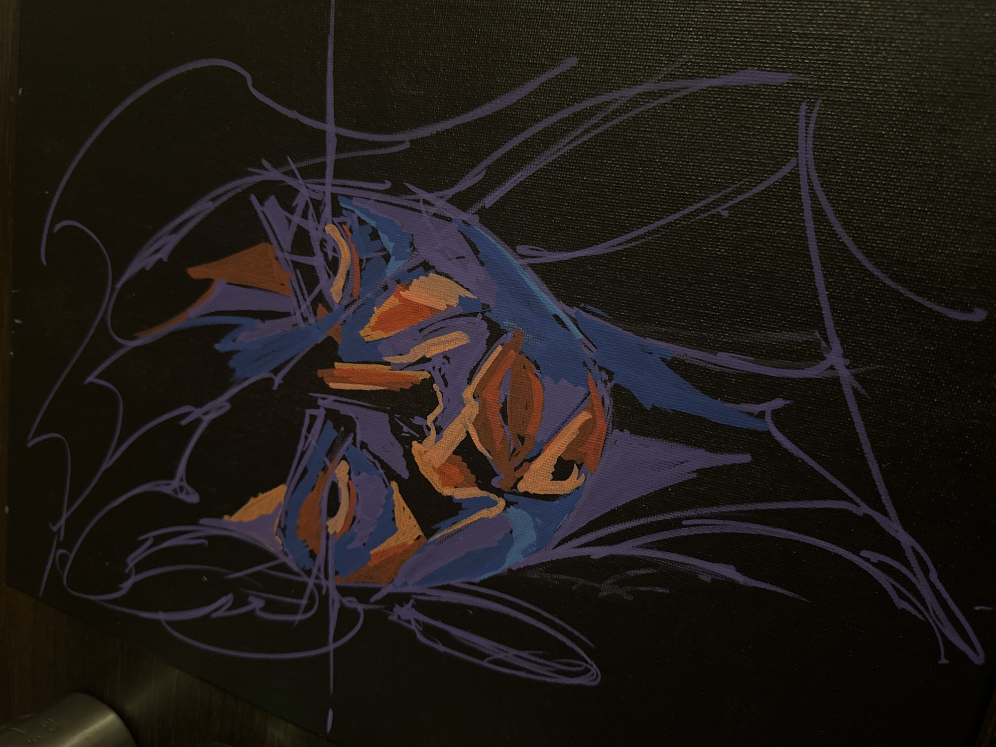The image shows a painting on a black canvas. The painting features abstract shapes and lines in shades of blue, purple, and orange. The central form appears to be vaguely bird-like, surrounded by a network of linear purple strokes that create a sense of movement or energy. The canvas has a textured surface. The background is dark, and only a small part of the wooden frame is visible. There is no indication of Sofia, Bulgaria.