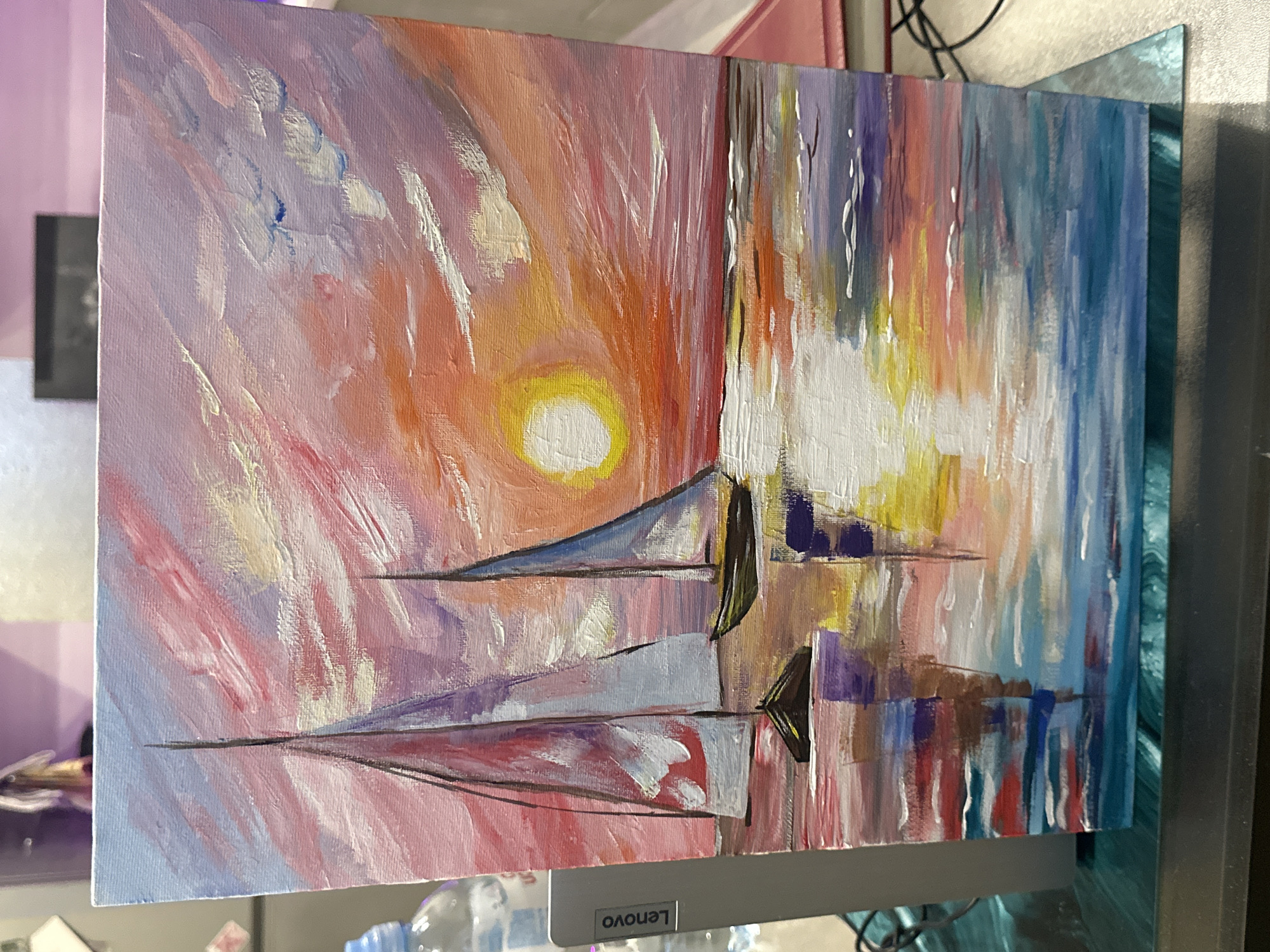 The image shows an abstract painting of sailboats on the water at sunset. The sky is a mix of pink, orange, and yellow, with the sun depicted as a bright yellow circle. The sailboats are rendered in shades of blue, purple, and white, with black lines outlining their shapes. Reflections of the boats are visible in the water, along with vertical strokes of color that suggest movement or light refractions. The painting is not located in any city or location.