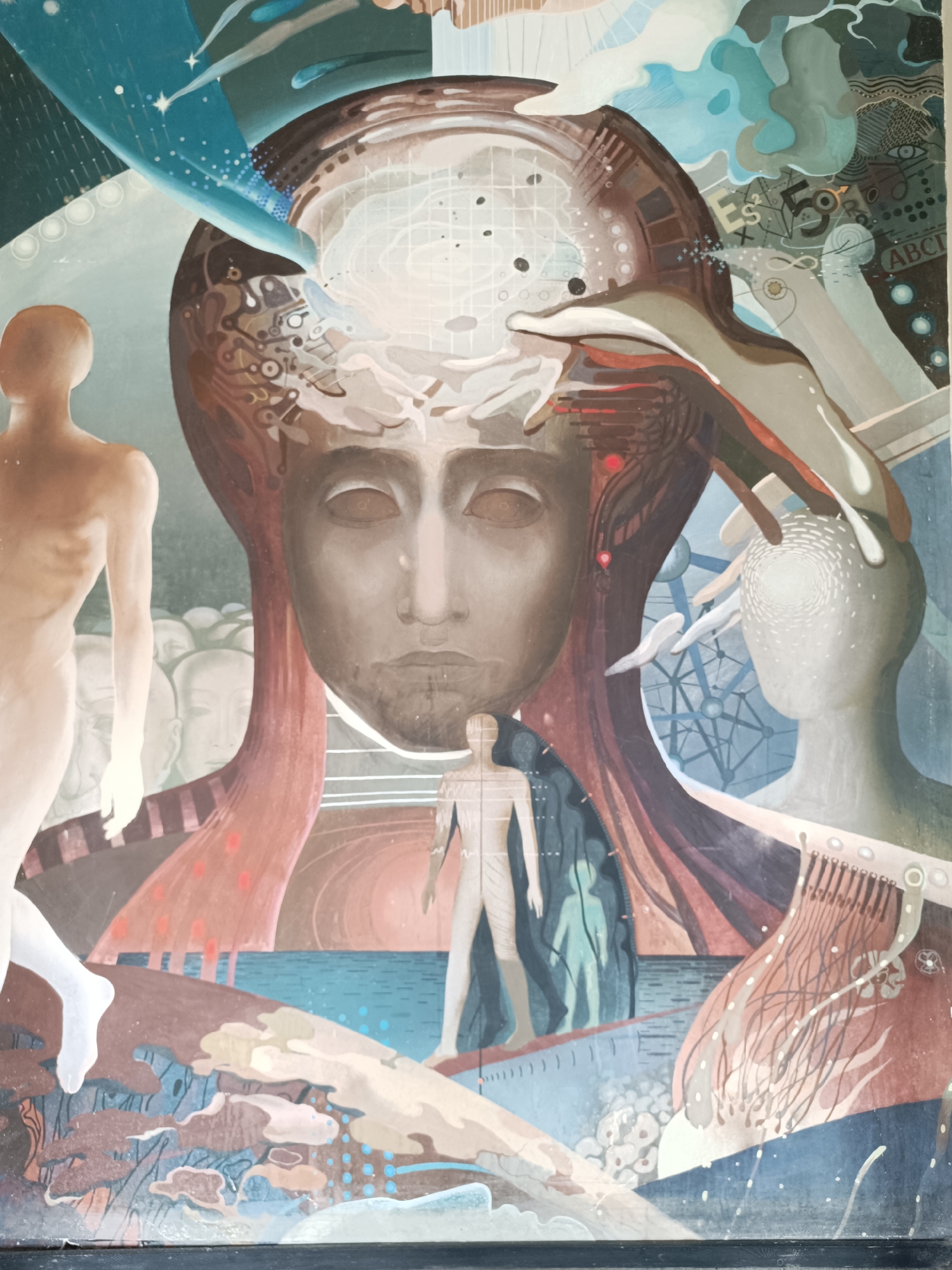 The image is a close-up photograph of a mural. The mural is figurative, depicting a large, central human face with eyes closed. The face is framed by a complex arrangement of symbolic elements including abstract shapes, figures, and geometric patterns.
On the left of the central face, a nude figure with back to the viewer is walking towards a crowd of faded figures. On the right, another abstracted figure with a pattern of white dots on its head and hands reaching towards it.
The mural has a variety of patterns, including a grid, mathematical formulas ("E=S^2/X"), the alphabet "ABC", and other abstract designs. The colors are muted, with a predominance of browns, blues, whites, and reds. The style is evocative of surrealism and incorporates elements of symbolism.
The mural is located in Sofia, Bulgaria.