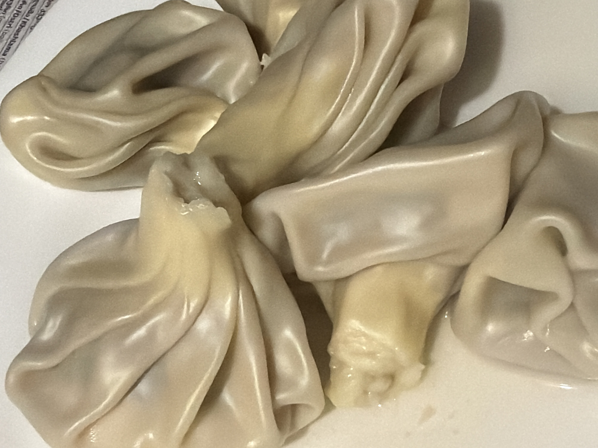 The image shows a close-up of several khinkali, a type of Georgian dumpling. The dumplings are pale, with visible folds and pleats in the dough. The filling inside appears to be meat, and the environment is likely a plate in a restaurant, given the popularity of khinkali in Tbilisi, Georgia. There are no people visible in the image.
