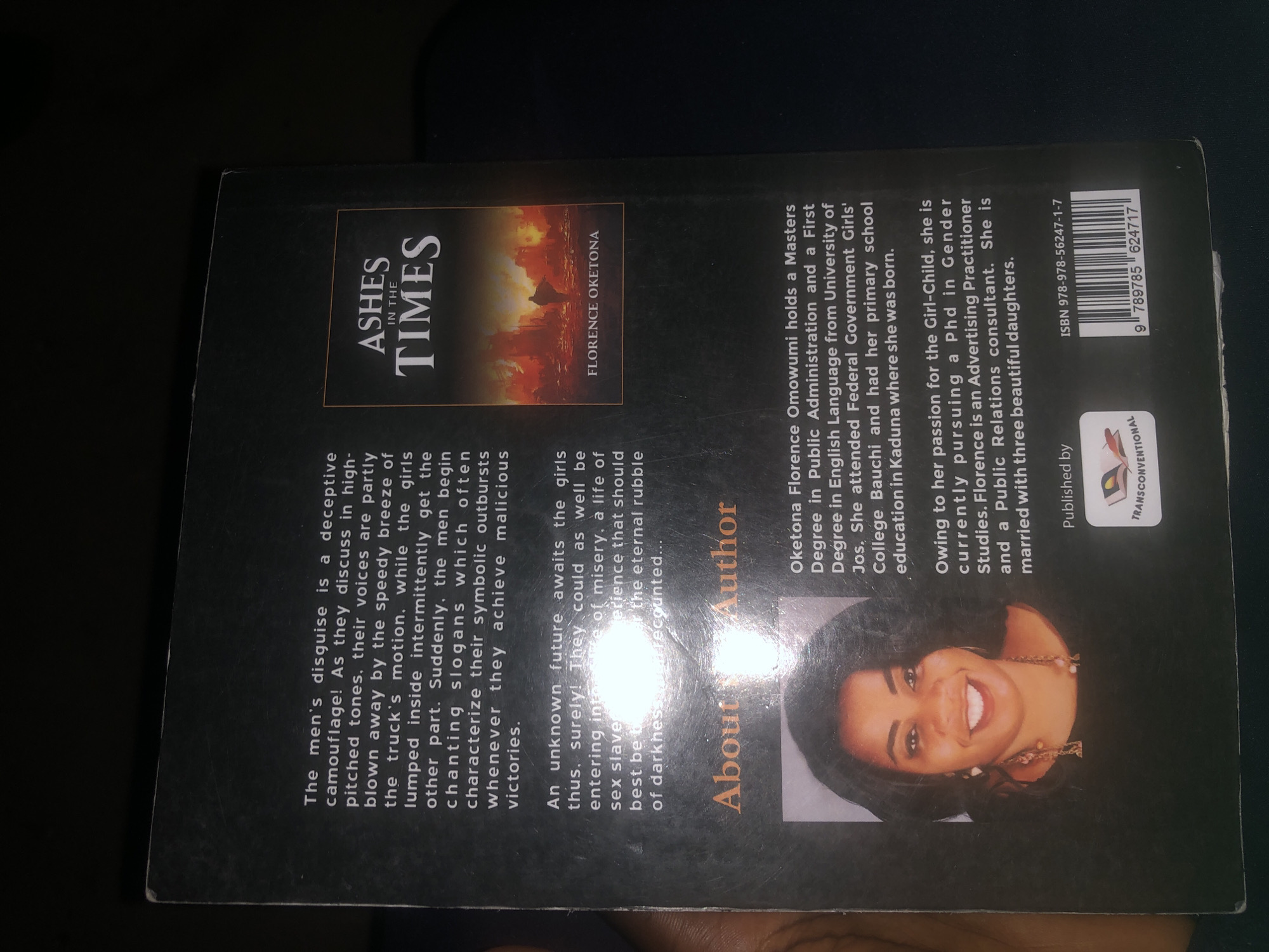 This is an image of the back cover of a book. The cover features text describing the book's plot and an author biography. The book title, "ASHES IN THE TIMES," is prominently displayed. The author's name, FLORENCE OKETONΑ, is also visible. There is a photograph of the author, a woman with dark hair, wearing earrings and a necklace, smiling. The author's biography states that she holds a Masters Degree in Public Administration and a First Degree in English Language. It also mentions her attending Federal Government Girls' College Bauchi and having her primary school education in Kaduna. The biography further states that she is pursuing a PhD in Gender Studies and is an Advertising Practitioner and Public Relations consultant, married with three daughters. A barcode and publisher information are also present. There is no information in the image that indicates the location in the city of Jalingo, Nigeria.