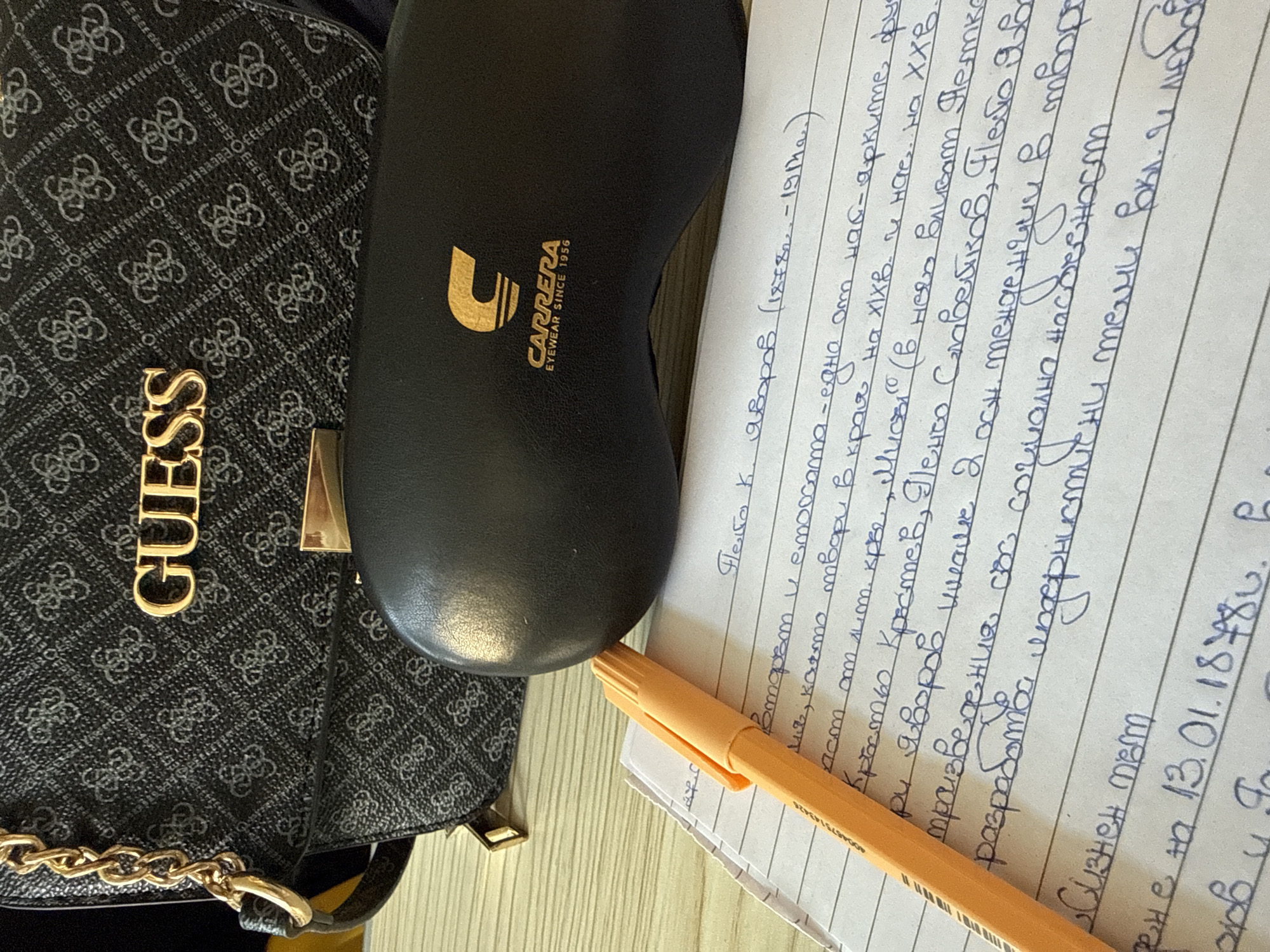 The image shows a Guess handbag, a Carrera eyewear case, a yellow highlighter, and a handwritten note on lined paper. The note is in Bulgarian and references the writer P.K. Javorov (1878-1917). It mentions several other names (Petko Slaveikov, Pencho Slaveikov), and refers to literary and social themes. There's a date on the note 13.01.18¥80. The setting is not revealed by the image.