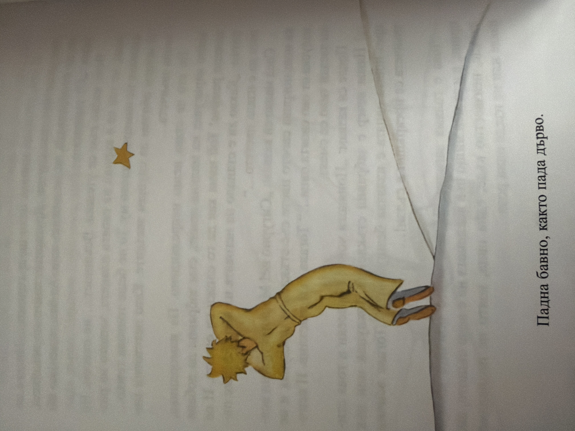 The image depicts a page from a book with an illustration and text. The illustration shows a boy with yellow hair, wearing a yellow outfit, standing on a white surface that appears to be a hill. He is leaning backward with his arms behind his head, and he is looking up at a small yellow star in the sky. The text below the illustration is in Bulgarian and reads: "Падна бавно, както пада дърво." This translates to "Fell slowly, as a tree falls." There is no information in the image that would indicate its location in the city of Pazardzhik, Bulgaria.