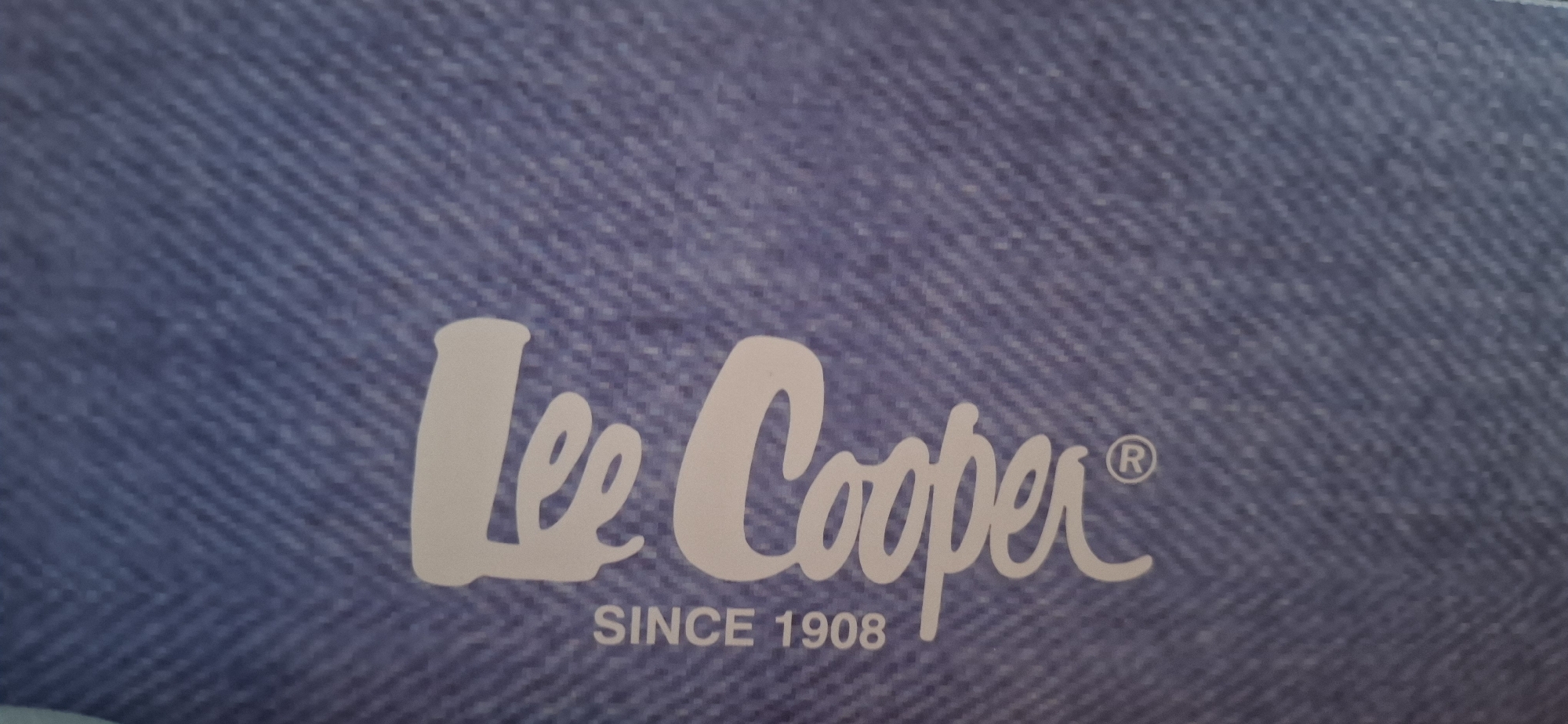 The image displays the "Lee Cooper" logo in white script against a blue denim background. Below the script, the text "SINCE 1908" is also present in white. The overall composition is a close-up shot of this branding. There are no people visible in the image. The provided context states this image is located in Yerocham, Israel, however, this specific geographical information cannot be visually verified from the image content itself.