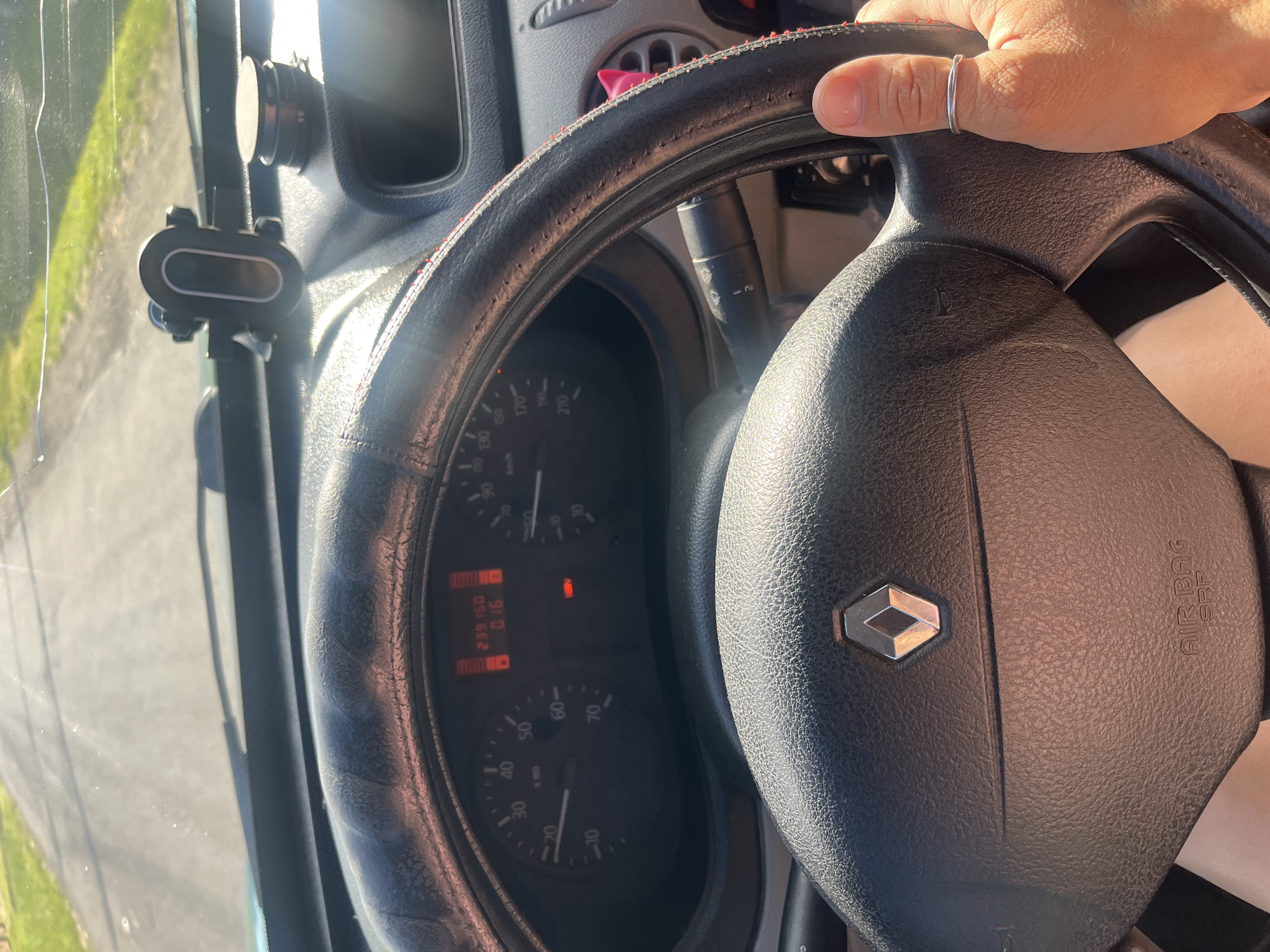 The image shows the interior of a car, as seen from the driver's perspective. The driver's hands are on the steering wheel. The dashboard displays various indicators, including speed and fuel levels. A phone mount is attached to the dashboard. Outside the car, a road and some greenery are visible. The scene appears to be in the city of Tarnivtsi, Ukraine, as suggested by the context.
