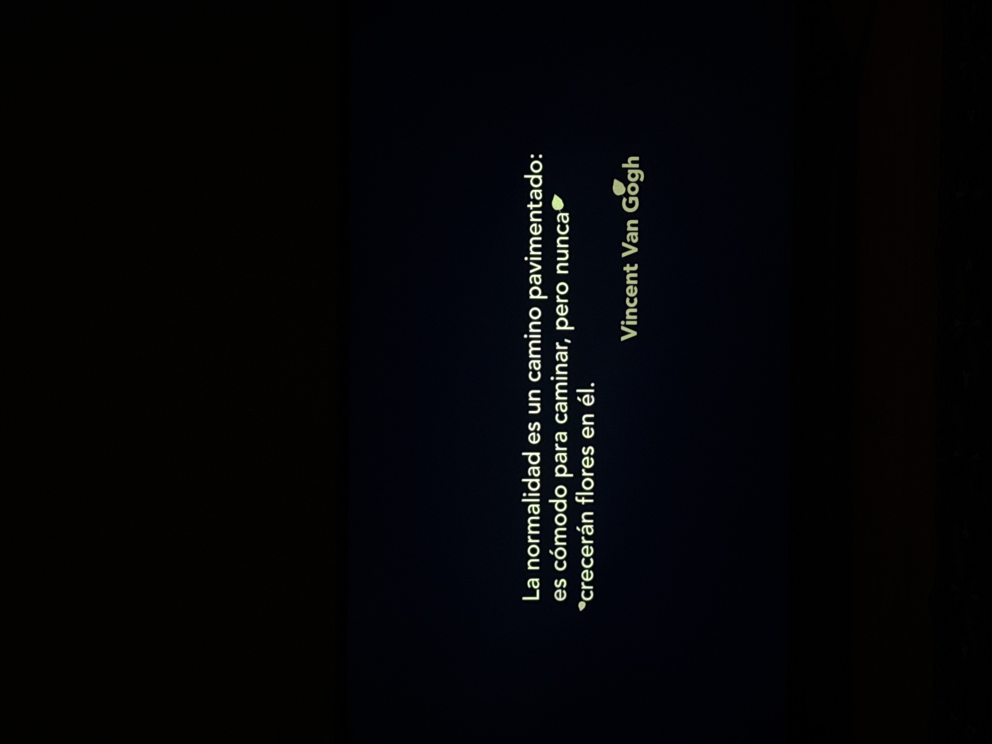 The image is a black screen with text in Spanish on the right side. The text is a quote from Vincent Van Gogh, which translates to "Normality is a paved road: it is comfortable to walk, but no flowers grow in it." The words are written in a light yellow color.