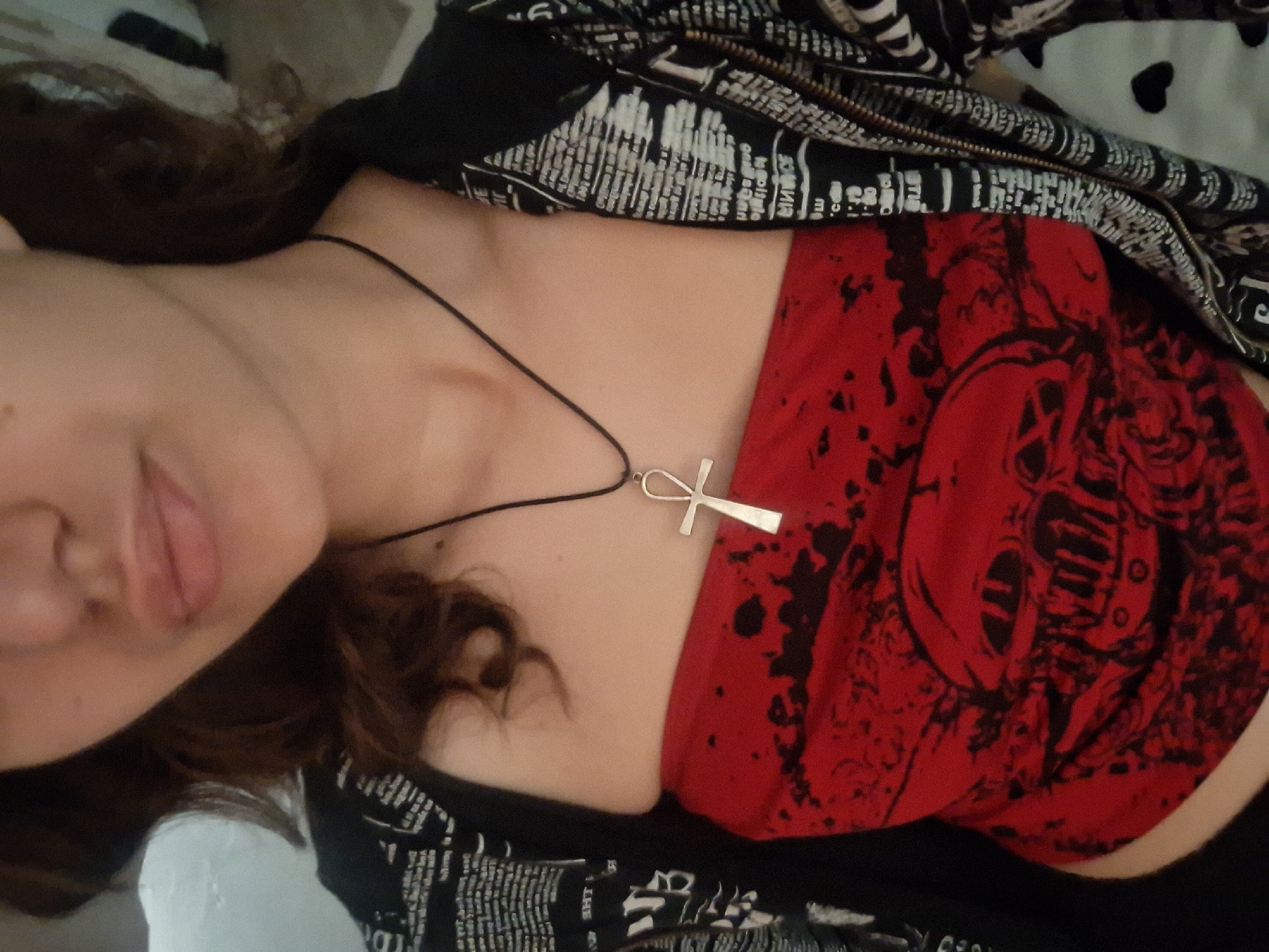 A woman with medium-length brown hair is visible in a close-up shot. She is wearing a red strapless top with a black skull design and a black jacket with white text. She has an ankh pendant necklace. The location is not discernible from the image, and there is no indication it was taken in Panagyurishte, Bulgaria.