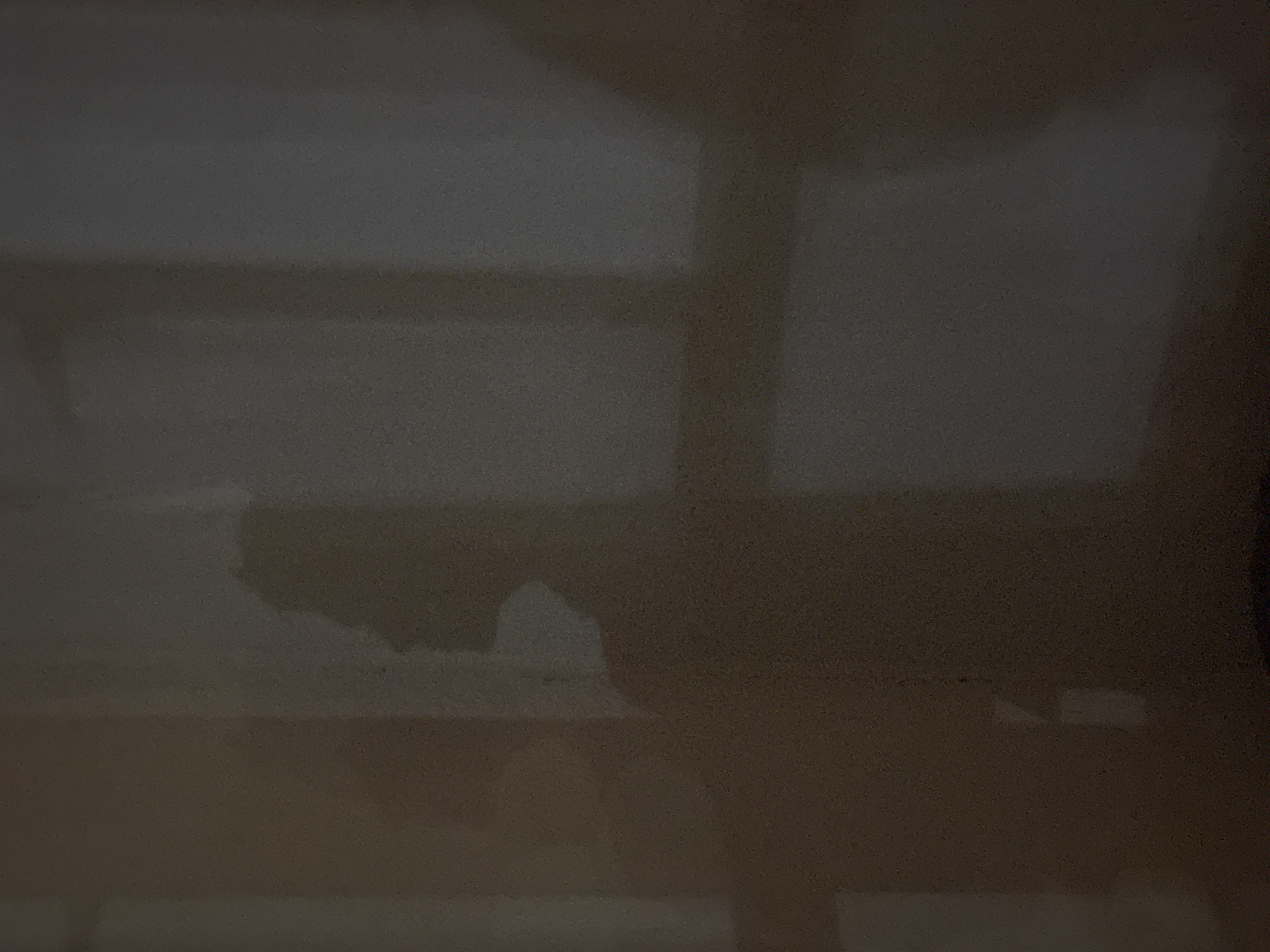 The image is a silhouette of a person's profile on a wall. The person is facing left, with their head tilted slightly upward. The silhouette is cast by a light source from the right, creating a shadow on the textured wall. The background is dimly lit, with vertical lines suggesting windows or door frames. The scene appears to be indoors, with the lighting creating a dramatic and somewhat mysterious atmosphere. No specific location in Sinyavino, Russia can be determined from the image alone.