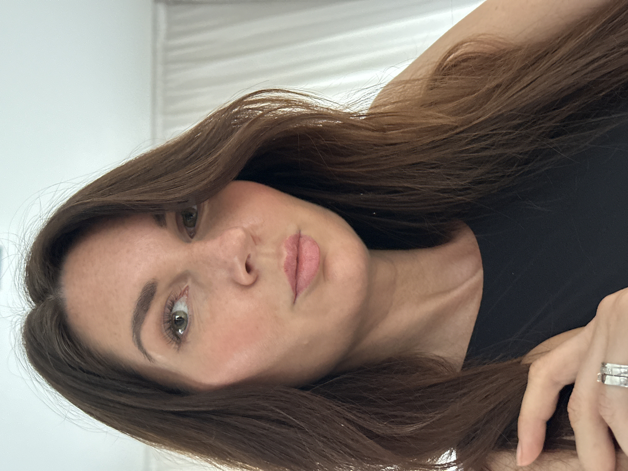 The image is a close-up, selfie-style shot of a woman with long, brown hair. She is wearing a black top and a ring on her left hand. Her makeup includes eyeshadow, blush, and lipstick. The background appears to be an indoor setting with white curtains. There is no indication of the city of Chaikovsky, Russia, or any specific location.