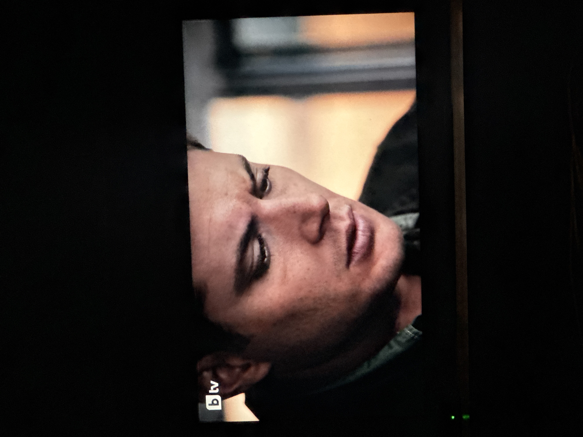 A screen displays a man's face in an apparent still from a BTV broadcast. The man has fair skin, dark hair, and closed eyes. He appears to be lying down. Behind him is a blurred background suggesting a vehicle interior. The BTV logo is in the bottom left corner of the screen. The surrounding environment is dark. There is no indication of Sarnevo, Bulgaria, or any forensic context.