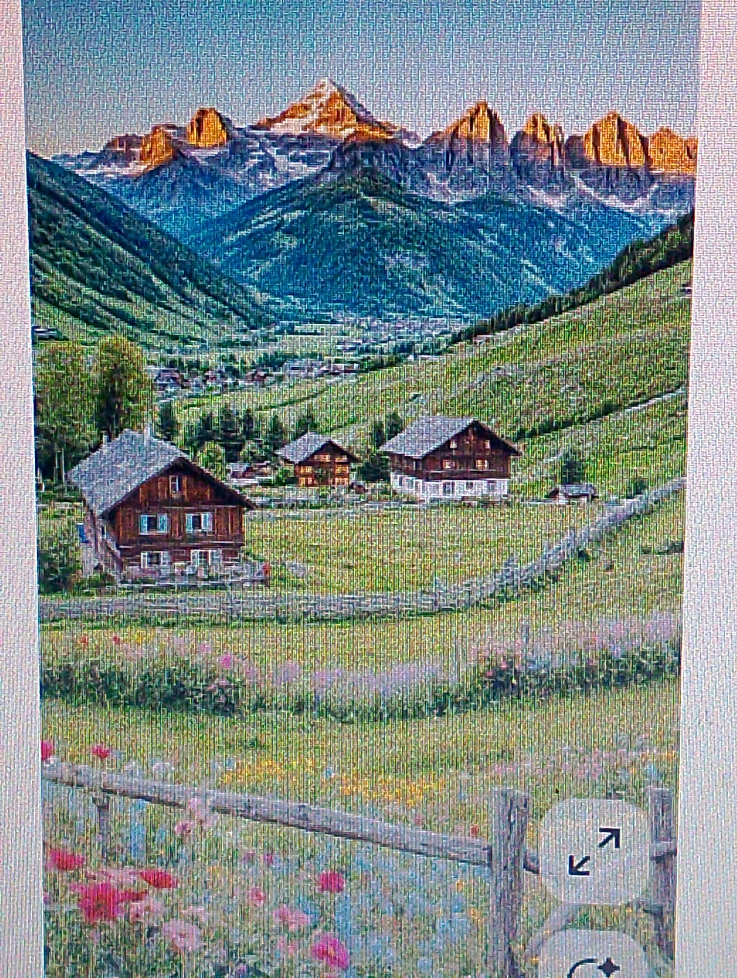 The image depicts a picturesque alpine village nestled in a valley, with towering, rugged mountains dominating the background. The mountains are snow-capped at their peaks and illuminated by the warm, golden light of what appears to be sunrise or sunset. The slopes of the mountains are covered in lush green vegetation, with a winding path visible in the mid-ground leading to a cluster of traditional wooden houses. These houses have dark wooden exteriors and lighter colored roofs, some with visible windows and balconies. In the foreground, a meadow is filled with colorful wildflowers, and a rustic wooden fence runs horizontally across the scene. The sky above is a clear blue, transitioning to a softer hue near the horizon. The overall impression is one of tranquility and natural beauty. There is no indication in the image that this scene is located in the city of Magelang, Indonesia.